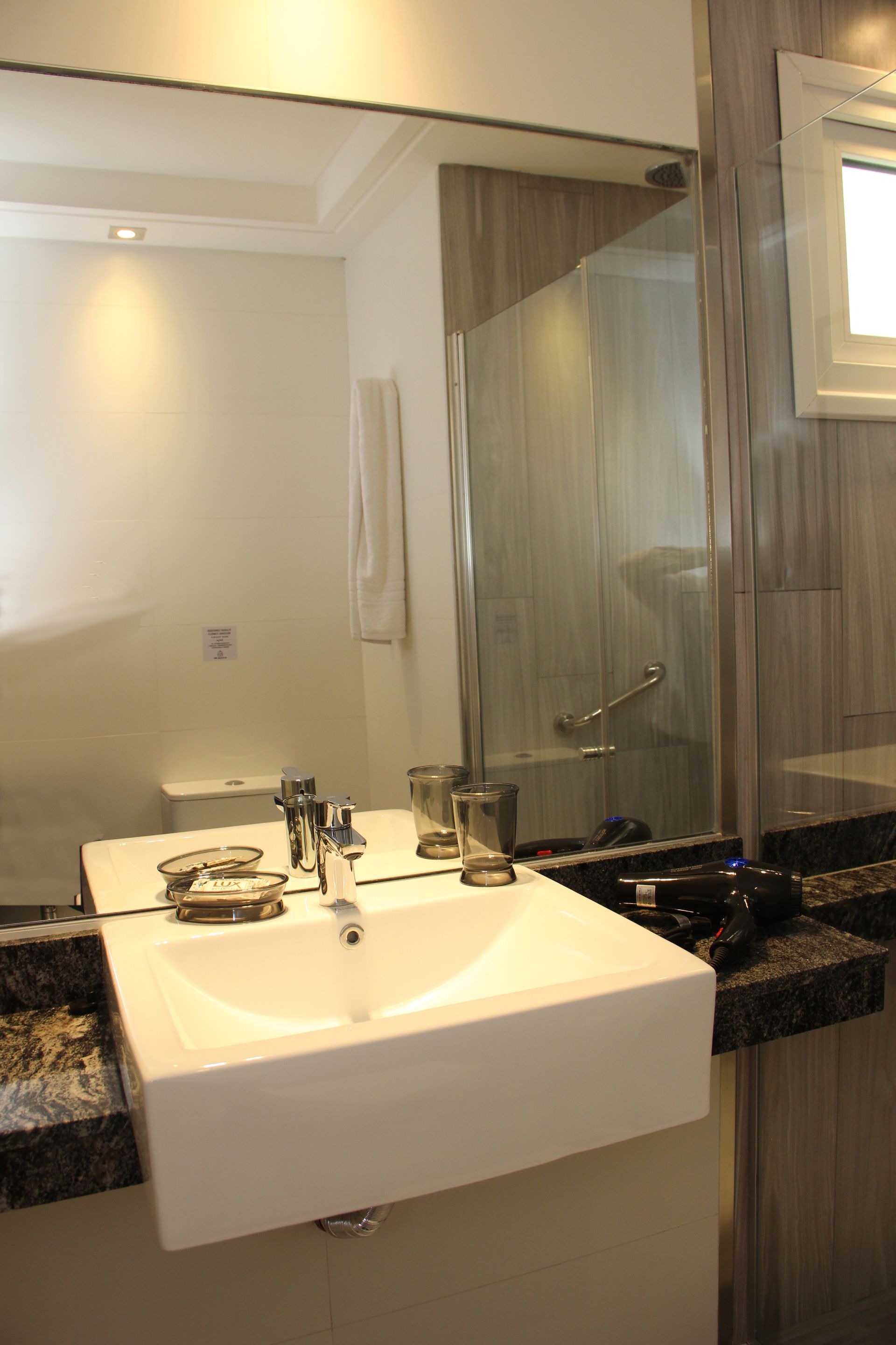 Modern bathroom vanity with white sink, mirror, glass shower, and granite countertop.
