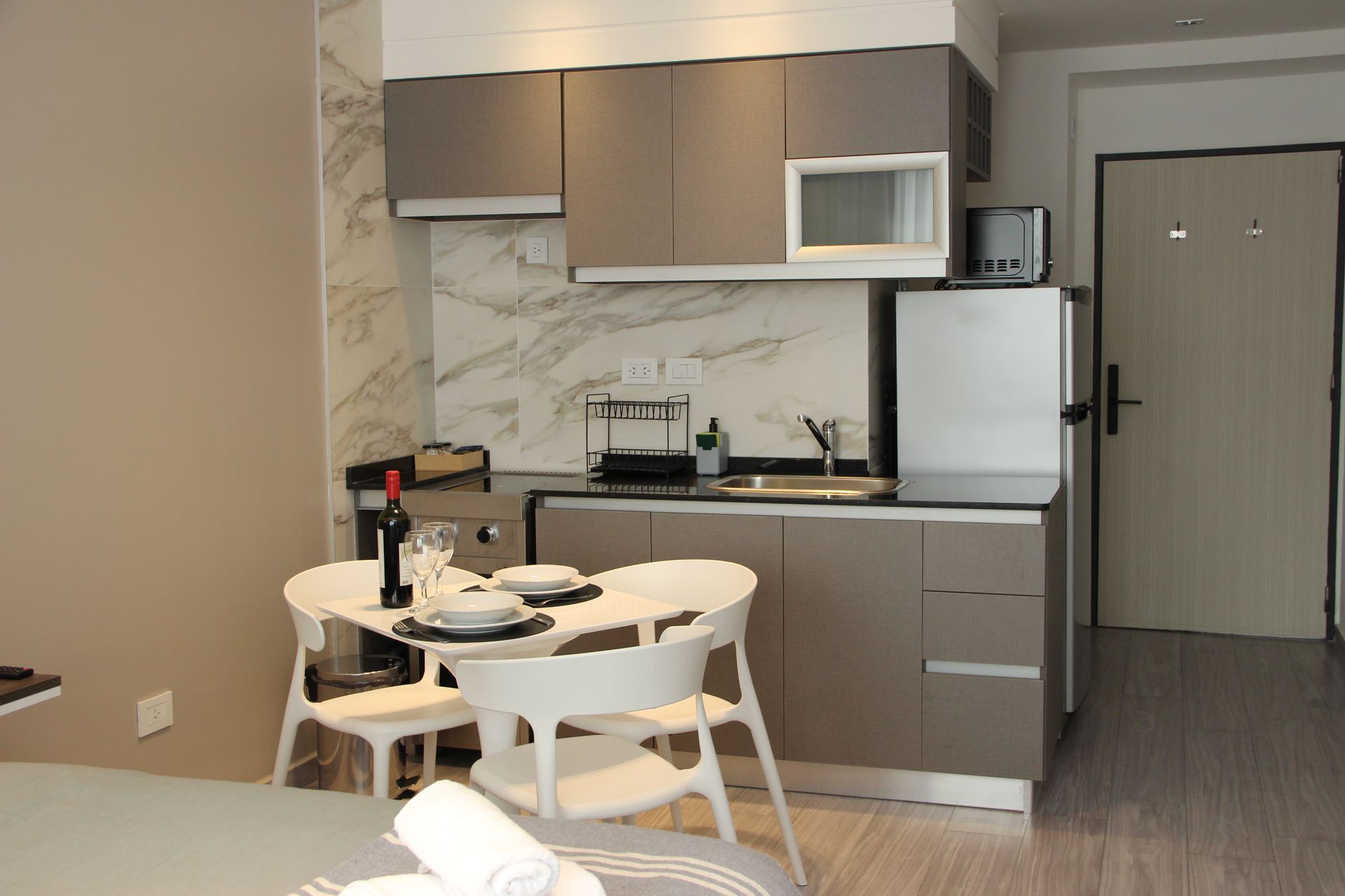 Compact kitchen and dining nook with white chairs, a round table, beige cabinets, and a refrigerator.