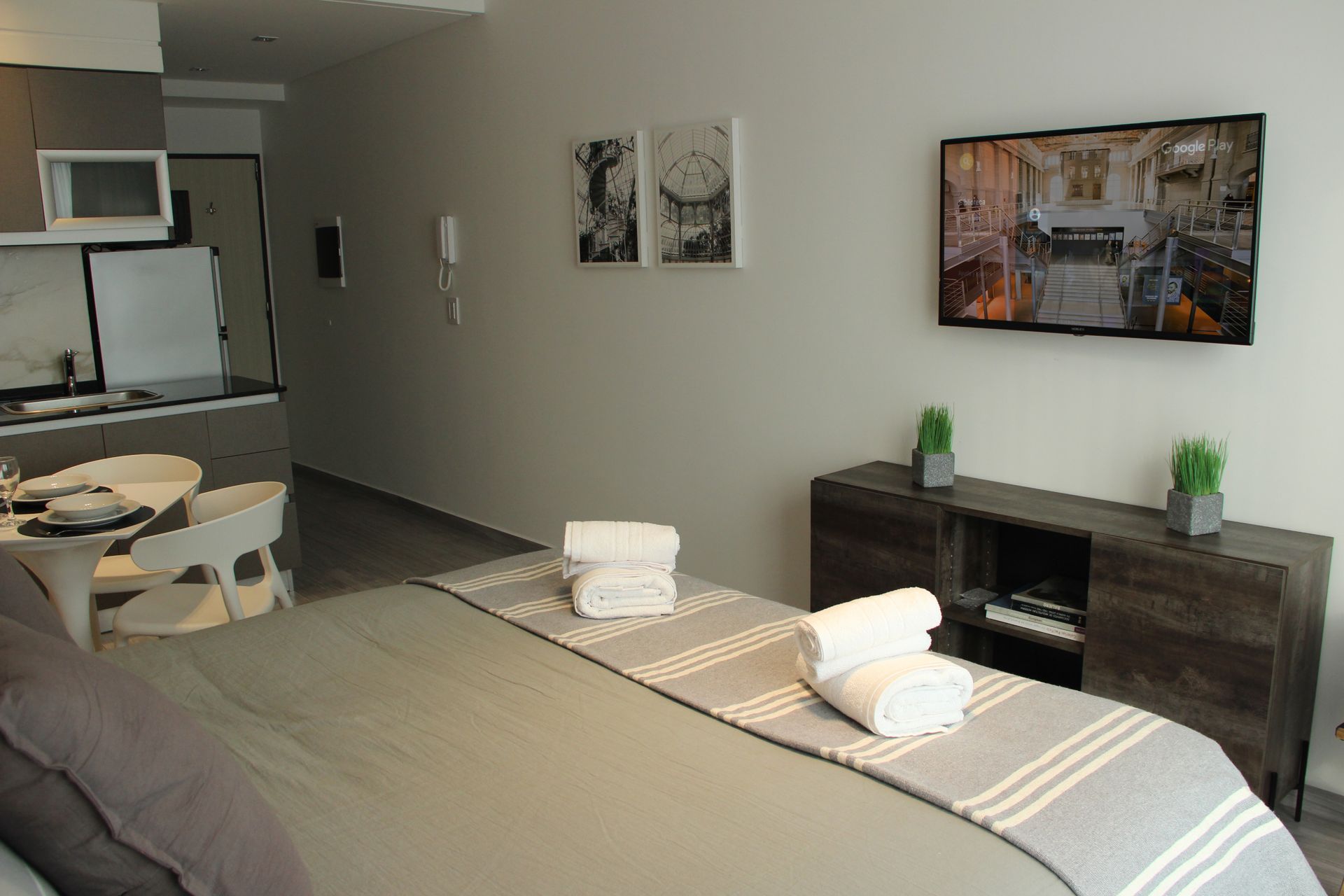 Modern hotel room with two beds, desk, wall art, and a small fireplace console