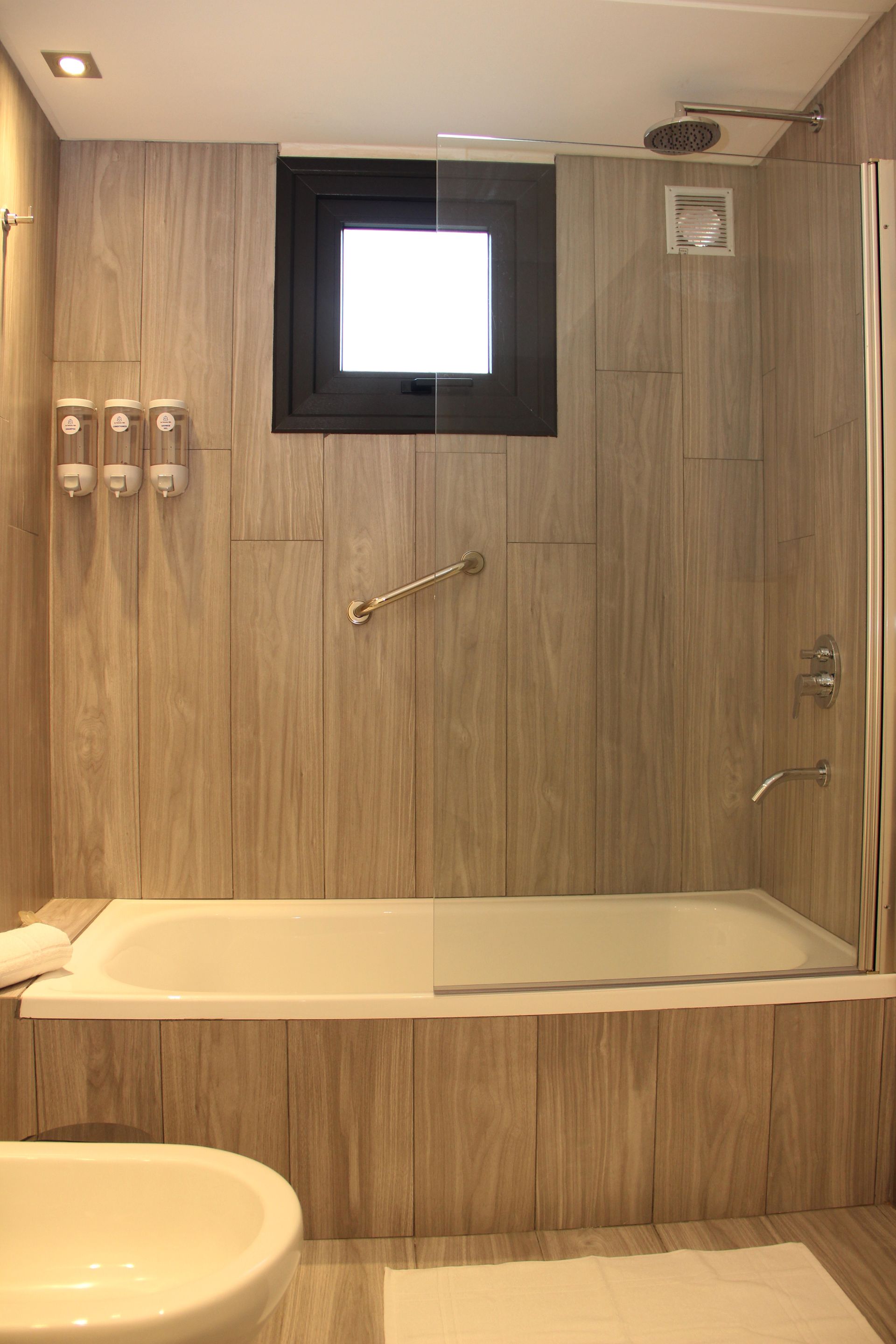 Wood-paneled bathroom with bathtub, sink, grab bar, and small window