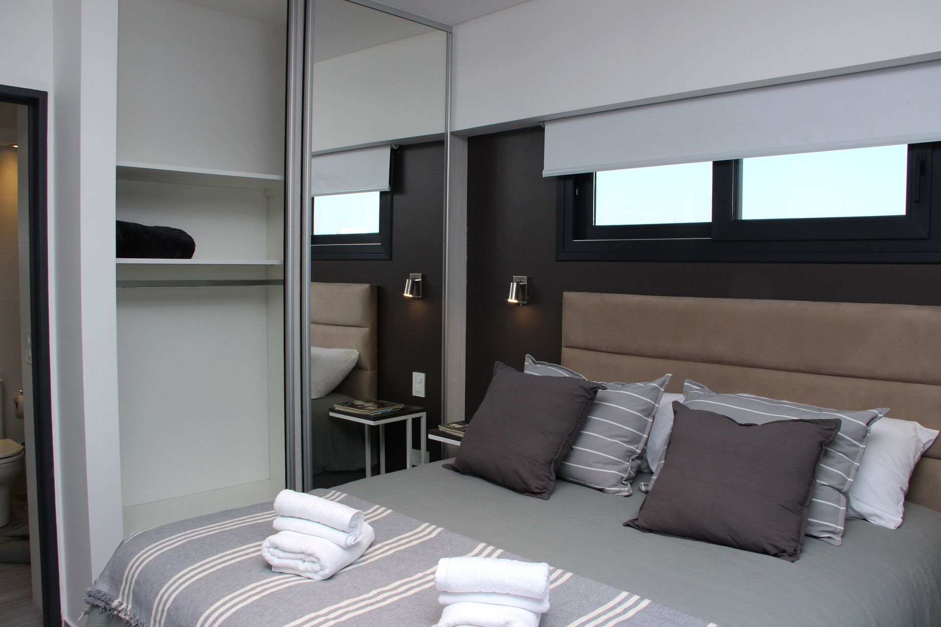 Modern bedroom with gray bed, pillows, mirrored closet, and small windows above the headboard