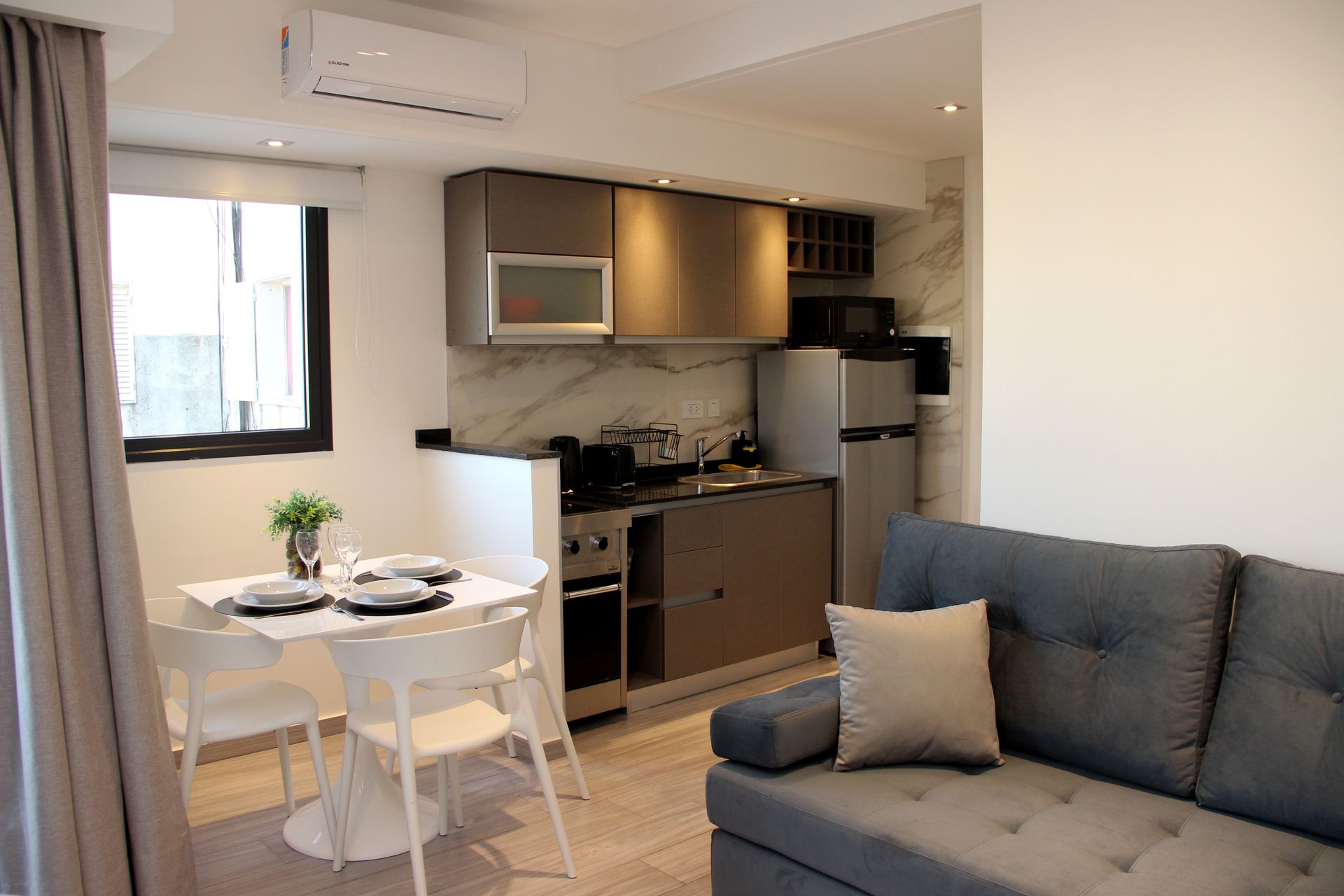 Modern apartment interior with a small dining table, compact kitchen, and gray sofa