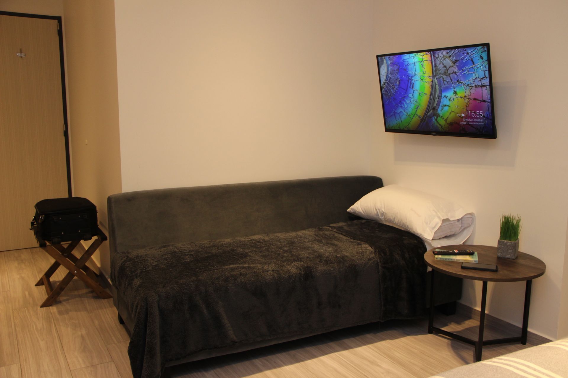 Cozy living room with gray sofa, wall-mounted TV, side table, and folding chair near a wooden door