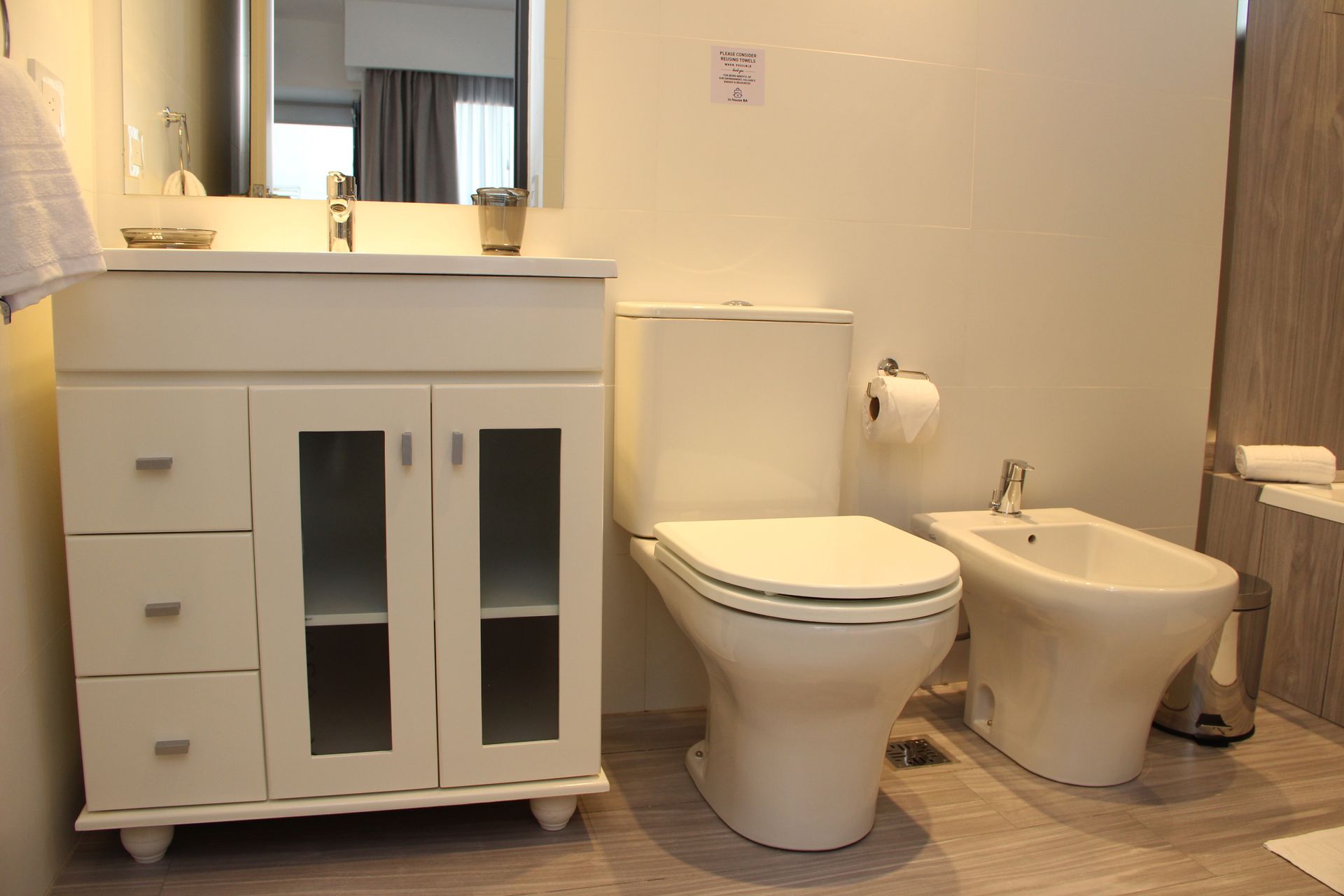 Bathroom with white vanity, toilet, and bidet on beige tile floor