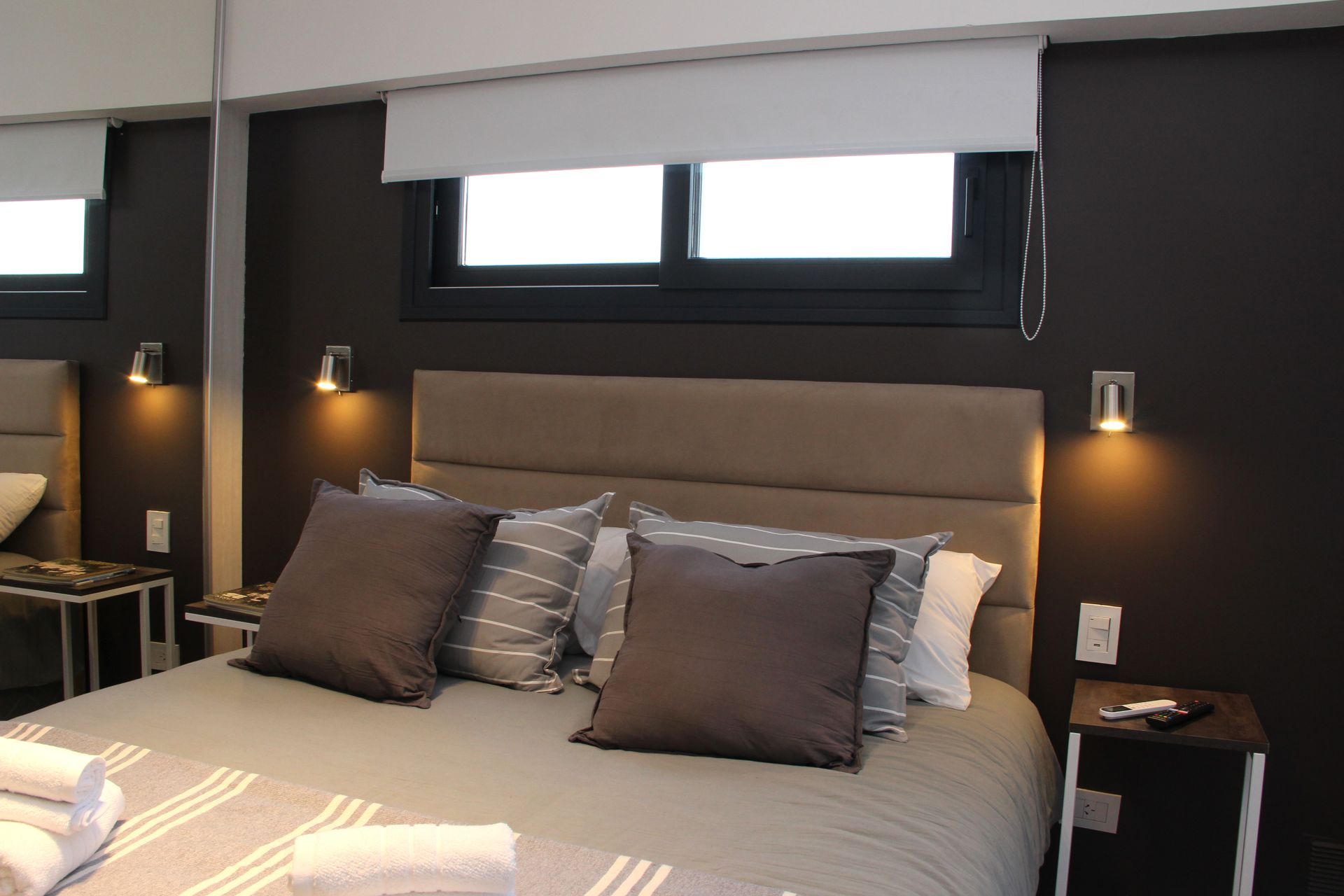 Modern bedroom with gray bedding, dark accent wall, wall lamps, and a headboard beneath a window