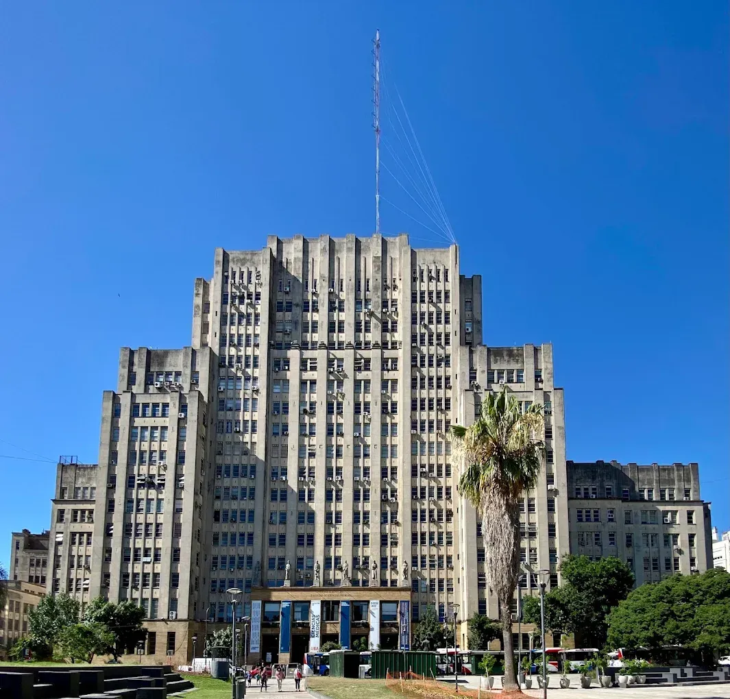 Art Deco city building with a central tower under a clear blue sky, framed by trees and a lawn