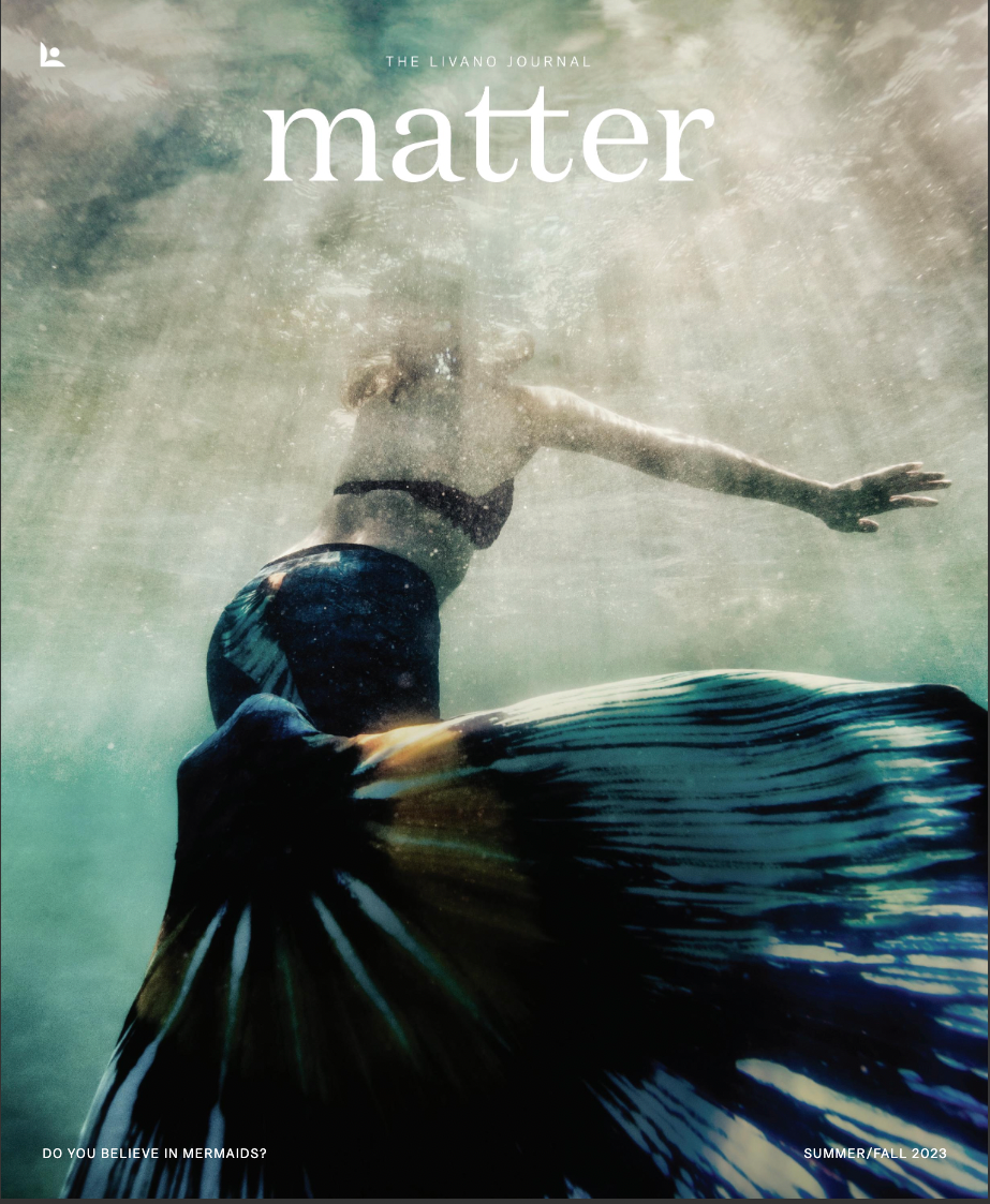 Woman in a mermaid tail underwater, reaching upwards. Pale light streams down.