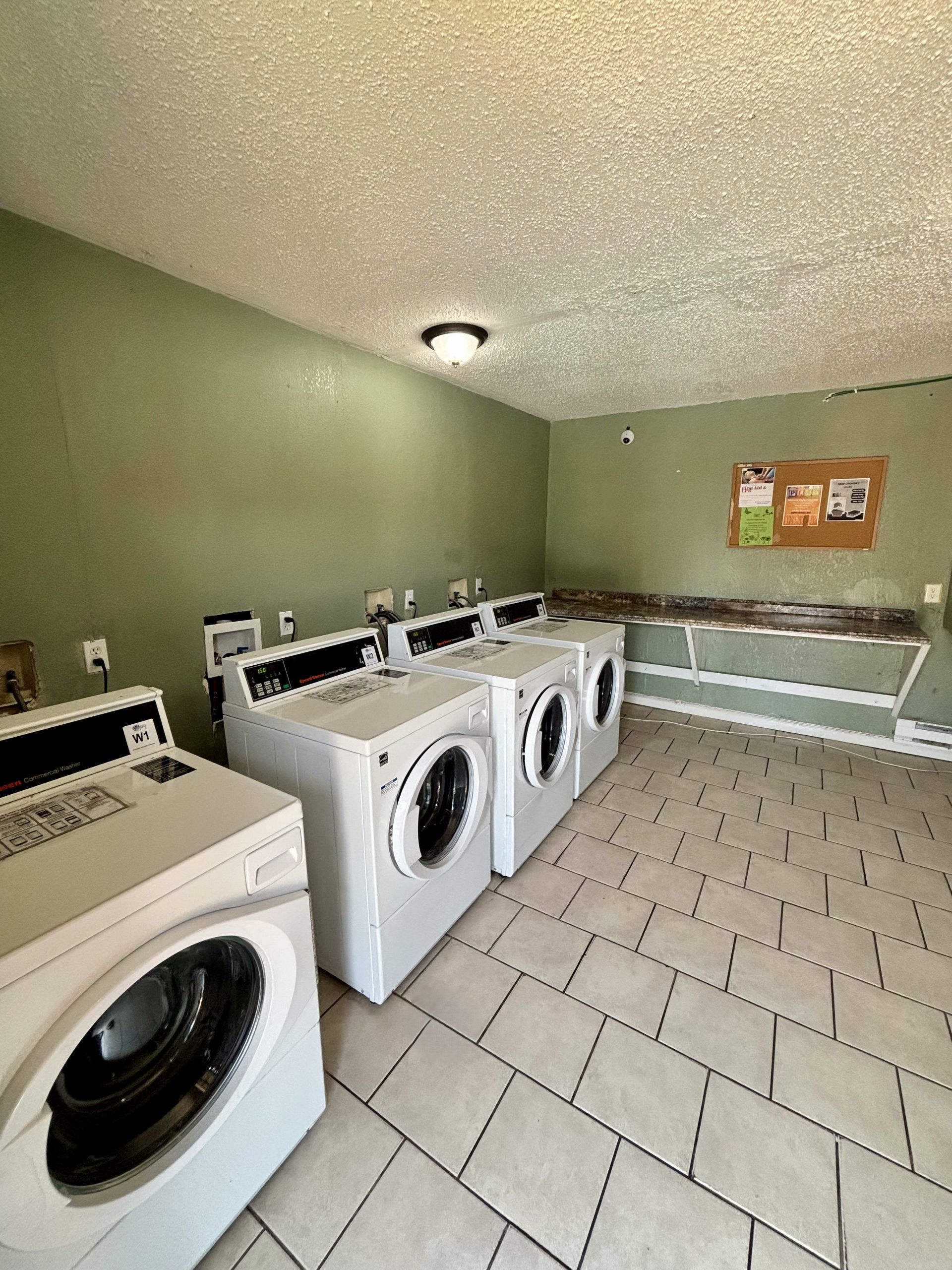 Laundry room with white washing machines, green walls, and beige tile floor.