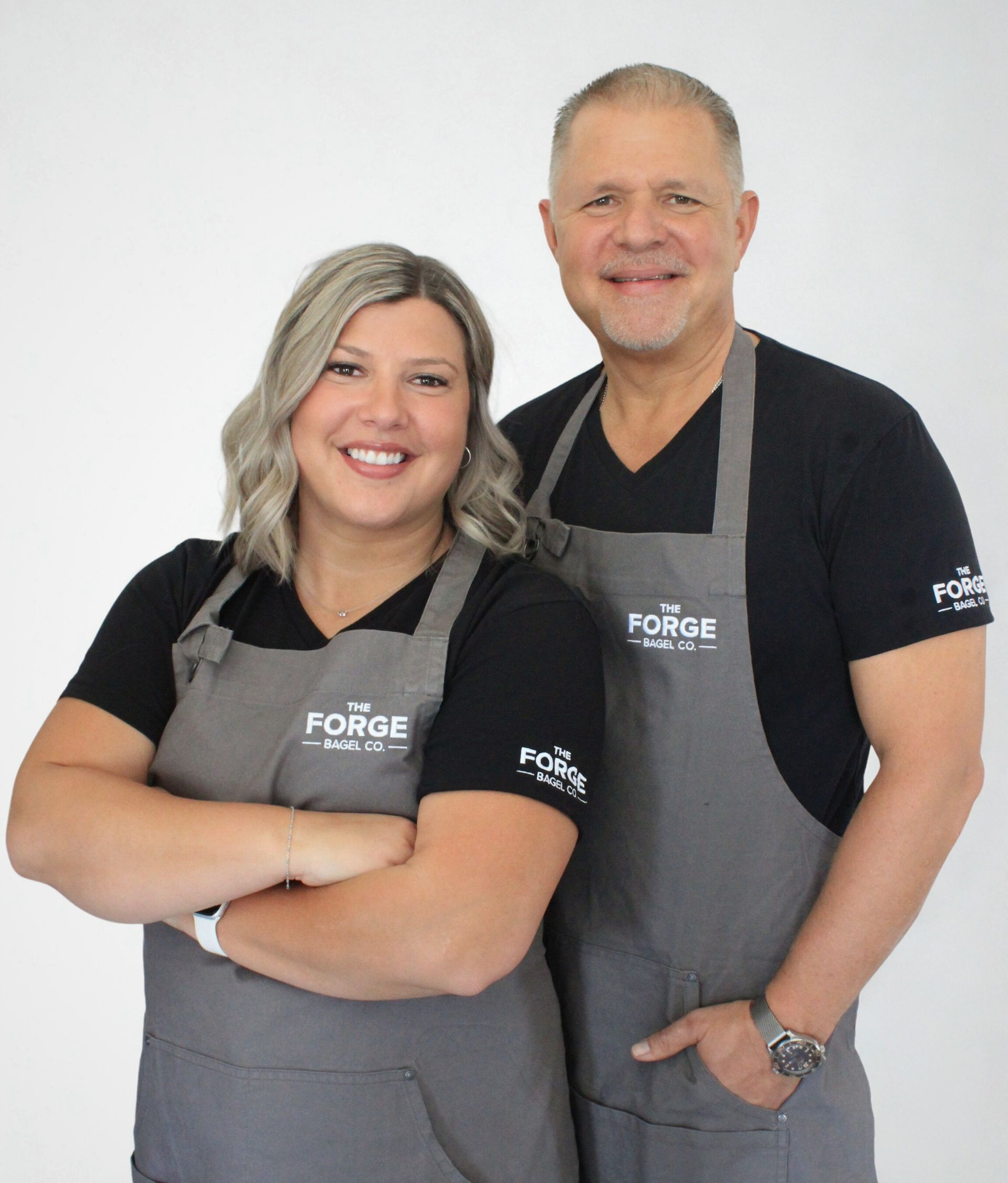 Glen and Rachelle wearing matching aprons, smiling at the camera. They stand in front of a white background.