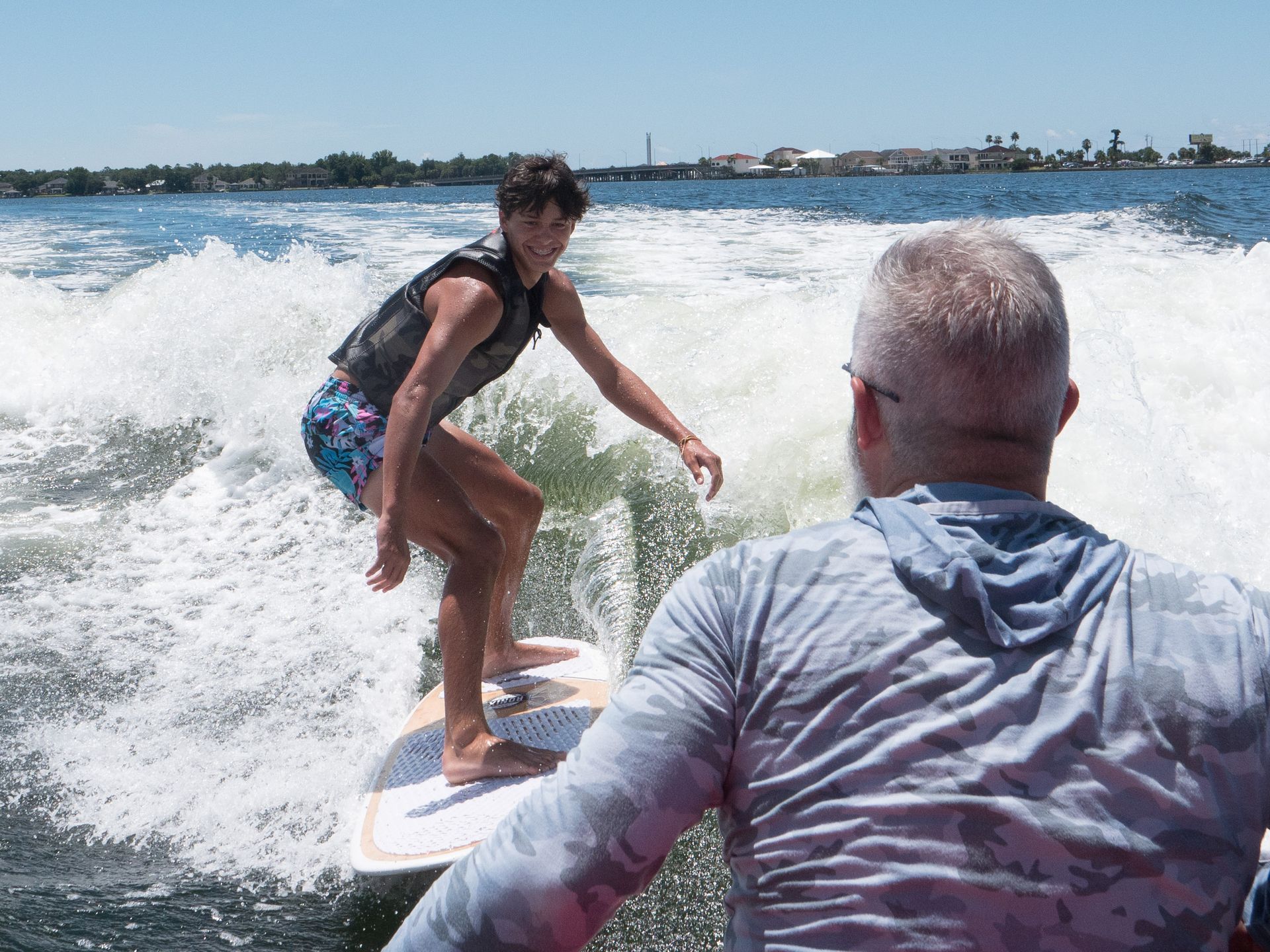 A man is watching a young boy riding a wave on a surfboard.