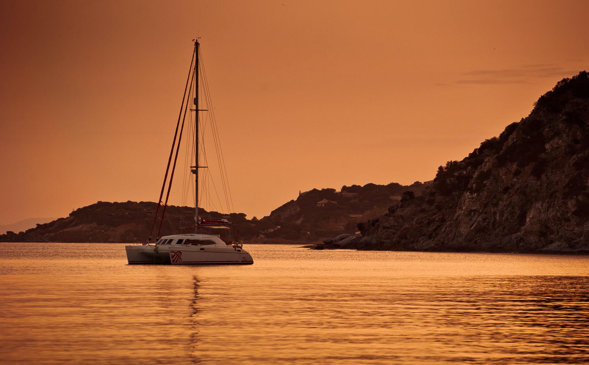 A sailboat is floating on top of a body of water at sunset.