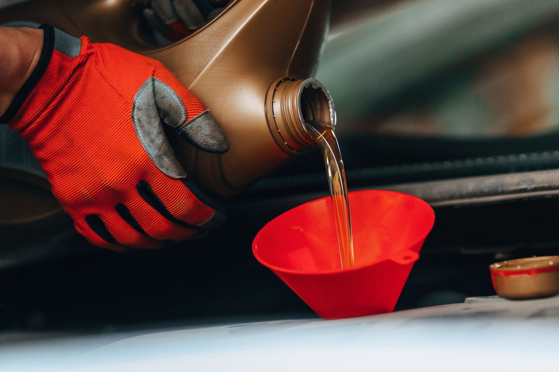 A person is pouring oil into a red funnel. A person is pouring oil into a red funnel.