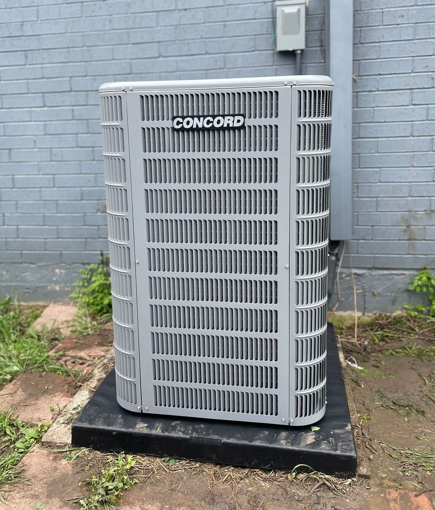 A concord air conditioner is sitting in front of a brick wall.