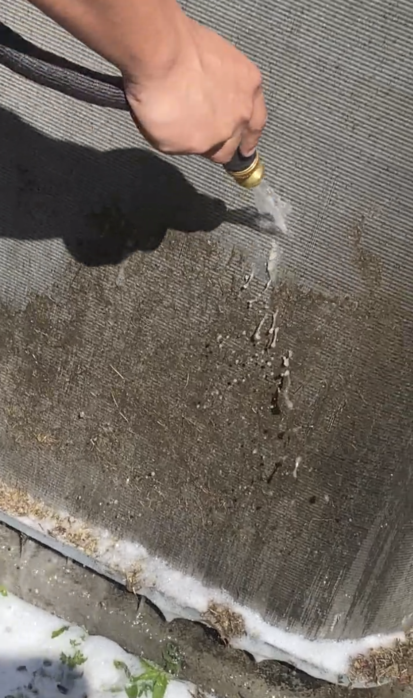 A person is spraying water from a hose on a condenser coil.