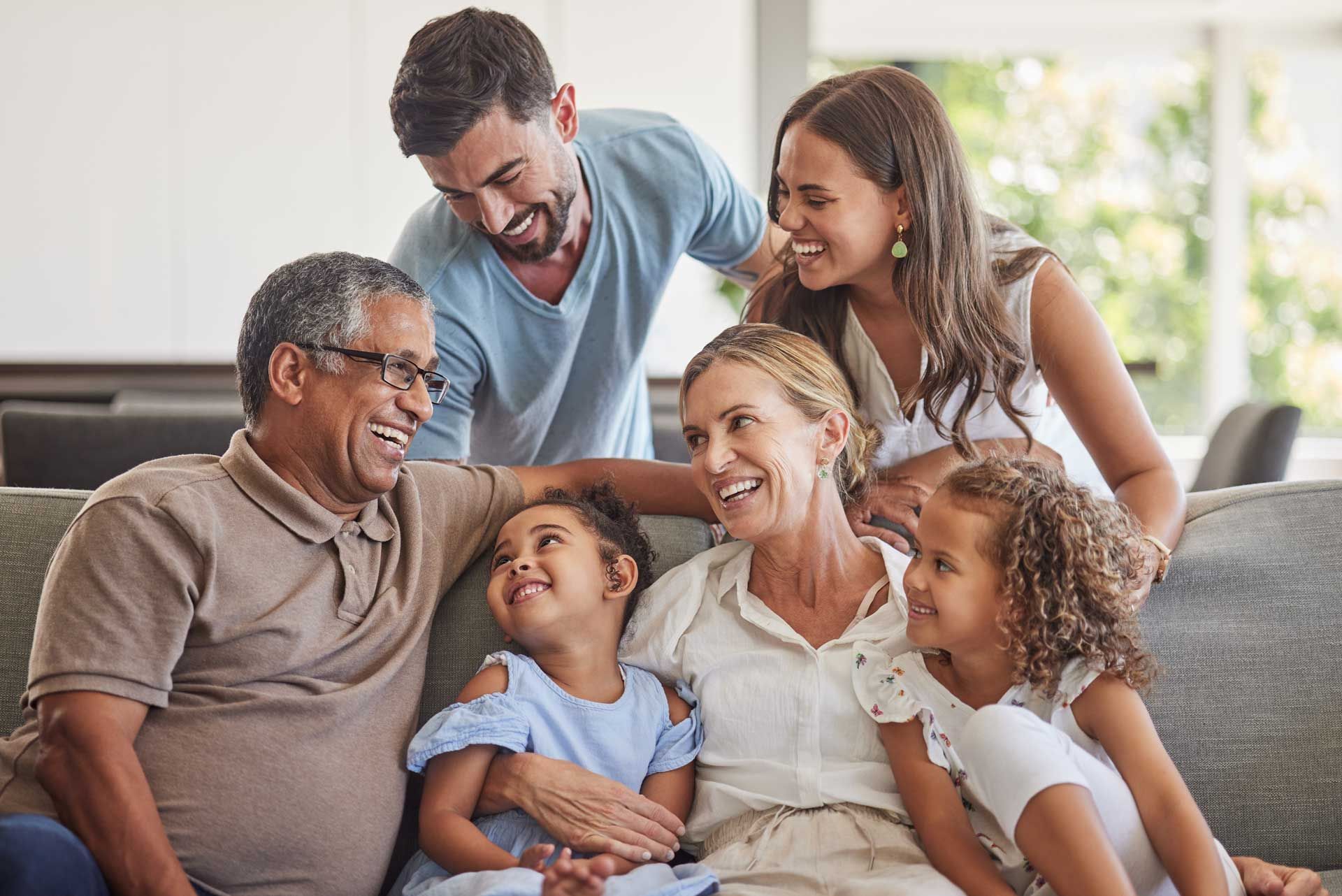 Family group smiles together on a couch. Man, woman, young girls, and two adults laughing. Family group smiles together on a couch. Man, woman, young girls, and two adults laughing.