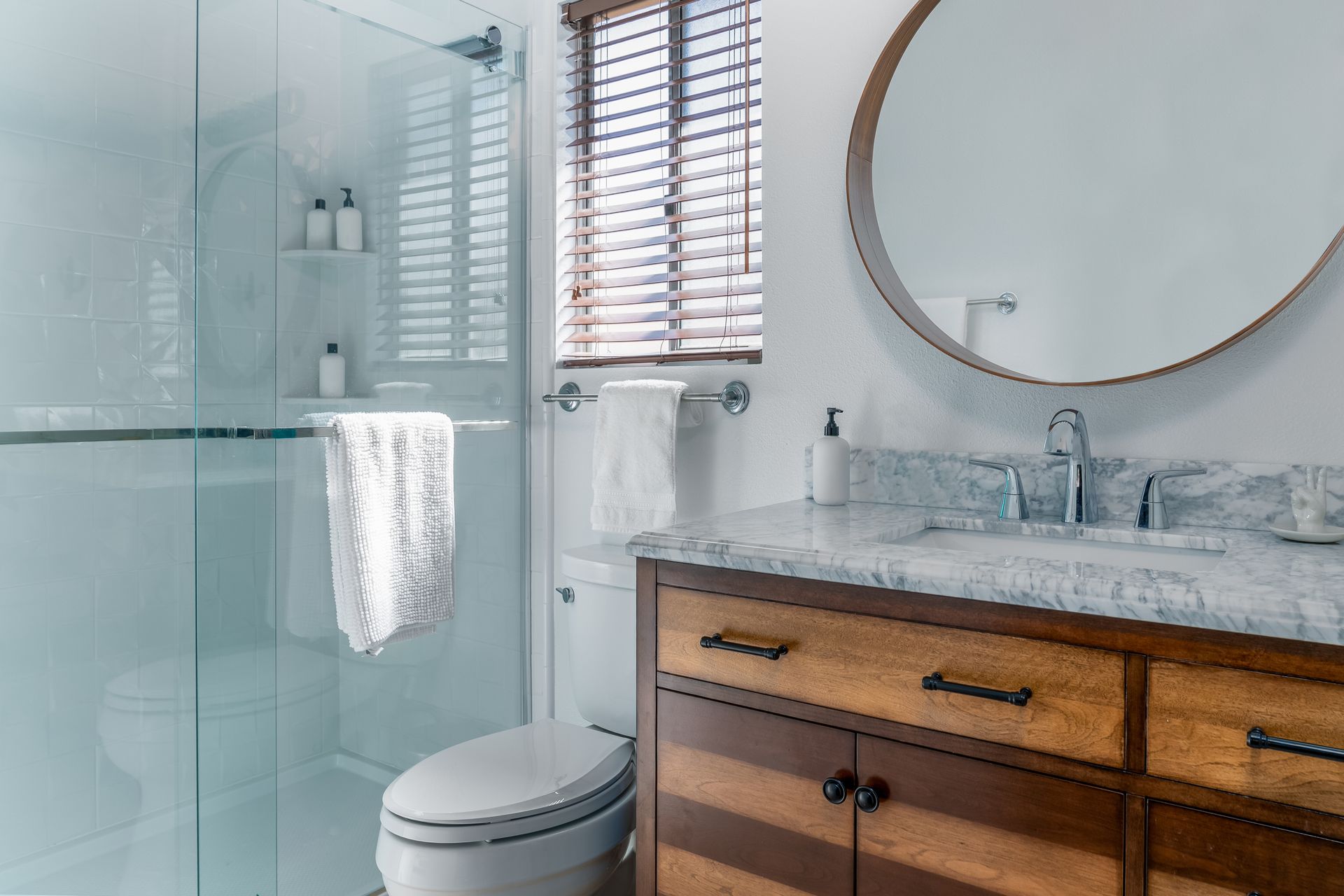 A modern bathroom with a glass-enclosed shower, a white toilet, a marble-topped vanity with wood cabinets