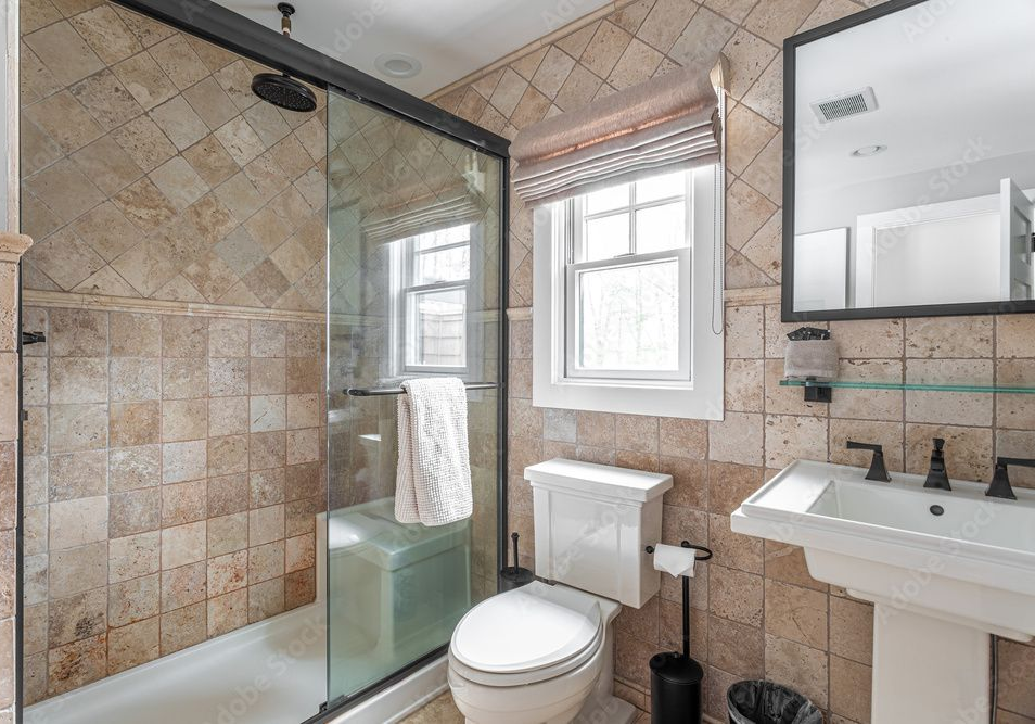 Bathroom featuring a walk-in glass shower, pedestal sink, toilet, and tan square tiles on the walls and floors.