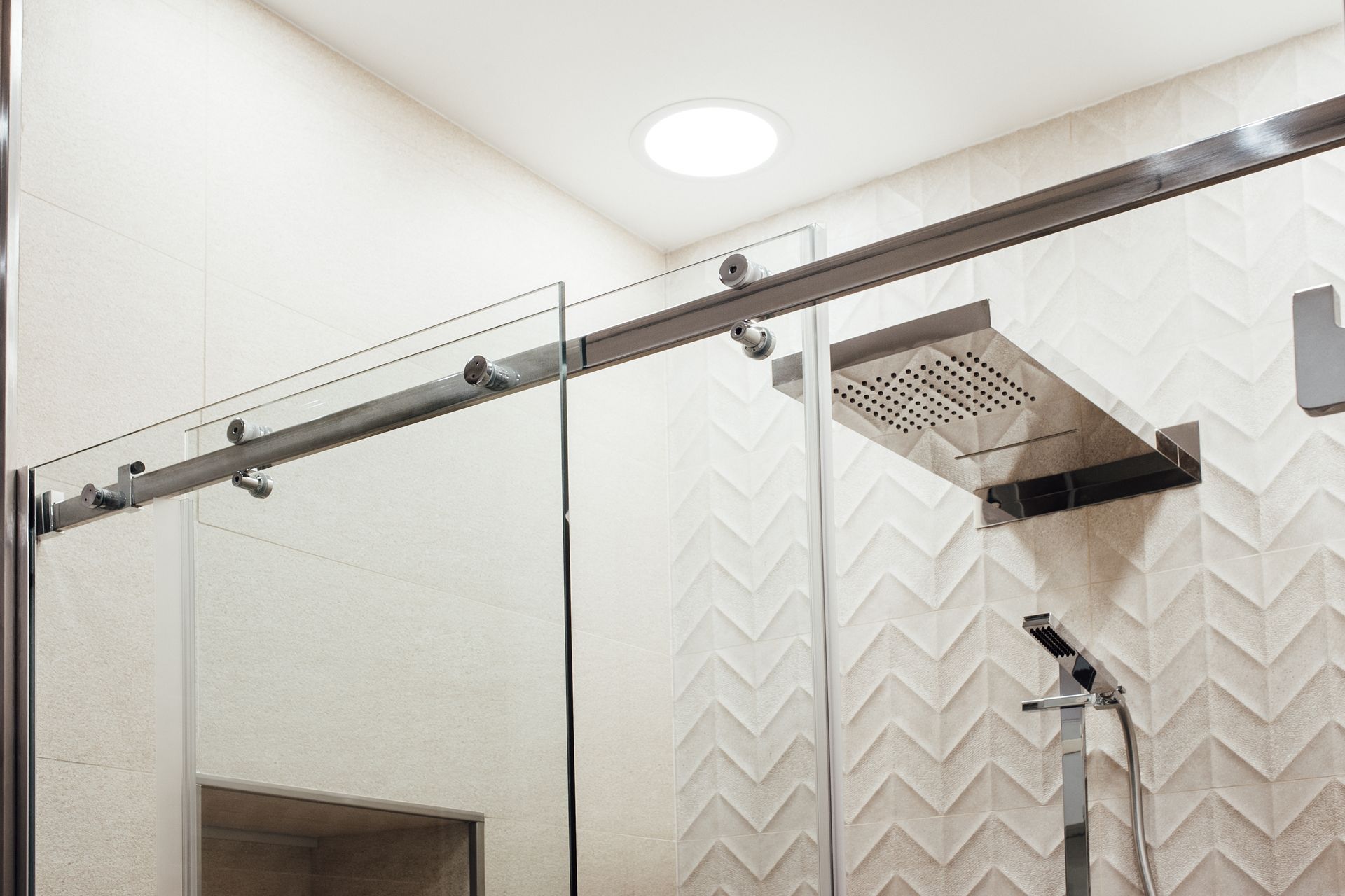 Modern walk-in shower with frameless glass door and square rainfall showerhead.
