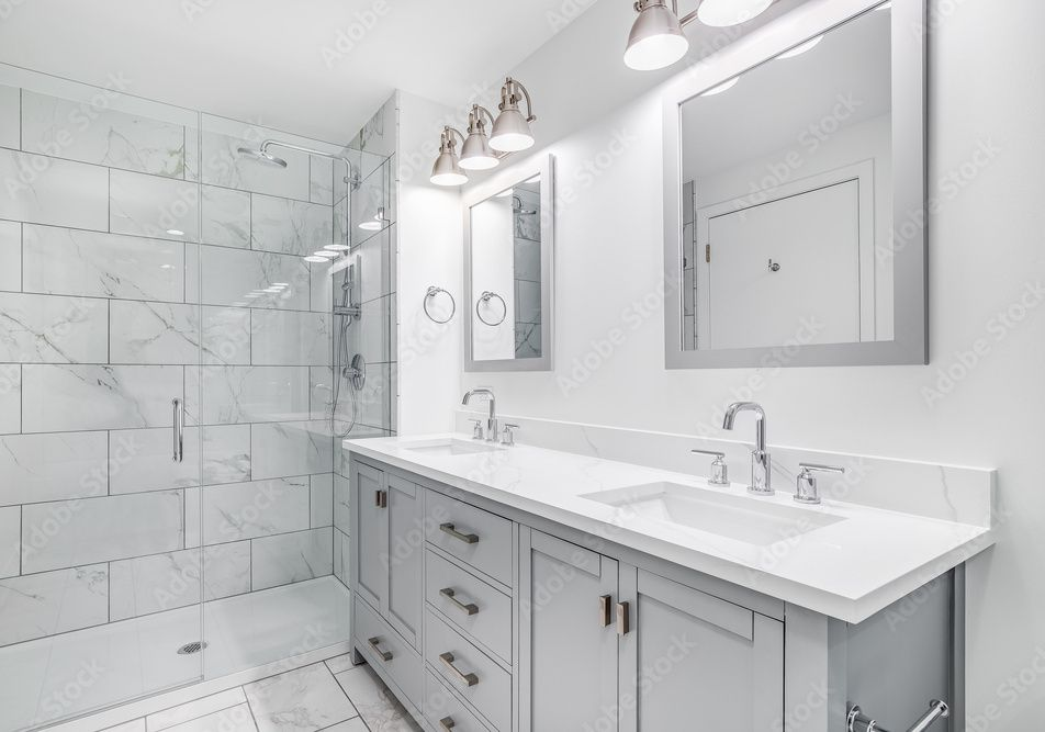 Modern bathroom with gray vanity, white marble-tiled shower, white countertops, and dual mirrors.