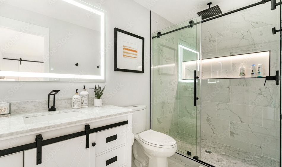 A modern bathroom with a marble vanity, black faucet, illuminated mirror, white toilet, and a glass-enclosed shower.