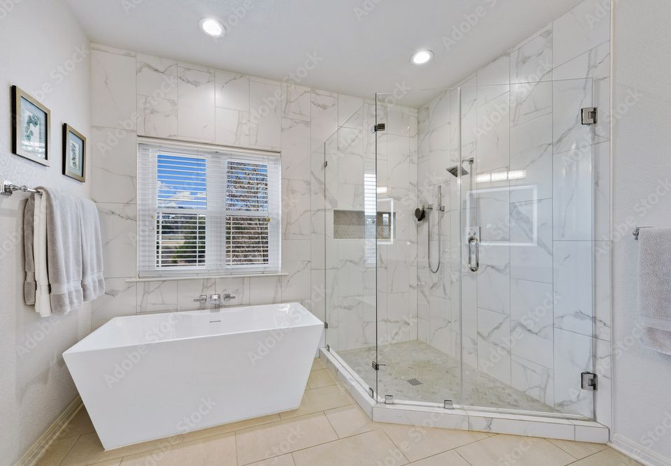 A modern bathroom featuring a white freestanding tub, a large glass-enclosed walk-in shower, and marble wall tiles.