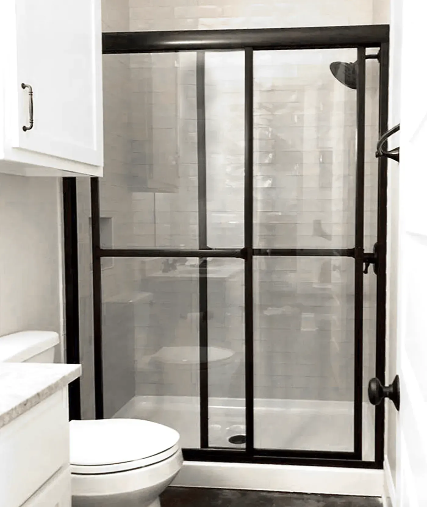 A modern bathroom with a glass-enclosed shower featuring a black frame next to a white toilet and cabinet.