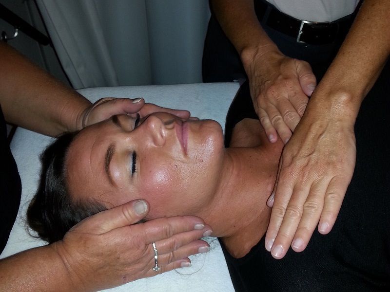Een persoon wordt door twee andere personen behandeld met Reiki op haar slapen en sleutelbeenderen.