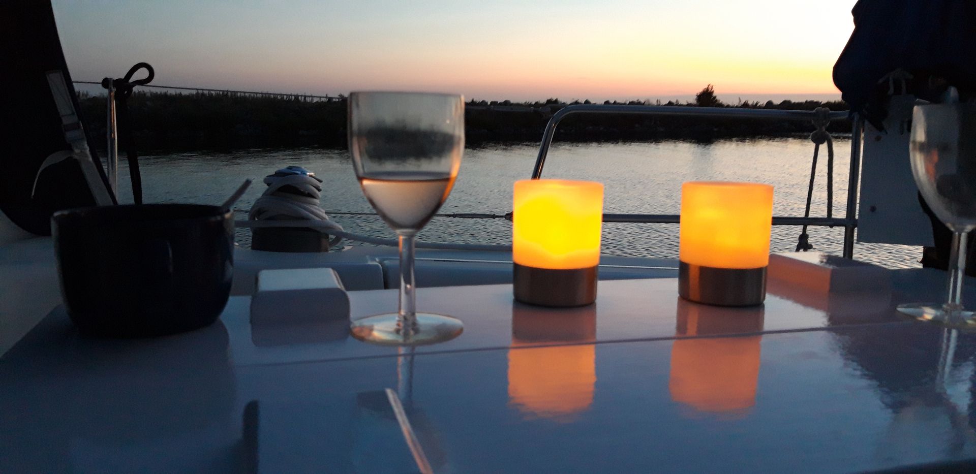 Tafel in de kuip van een zeilboot met een glas wijn en twee sfeerlampjes.