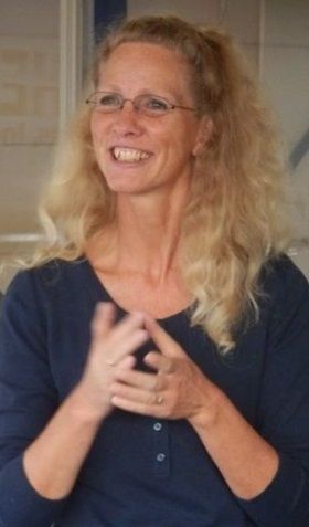 Anita enthousiast lachend tijdens het geven van een uitleg aan een (niet zichtbare) groep mensen.