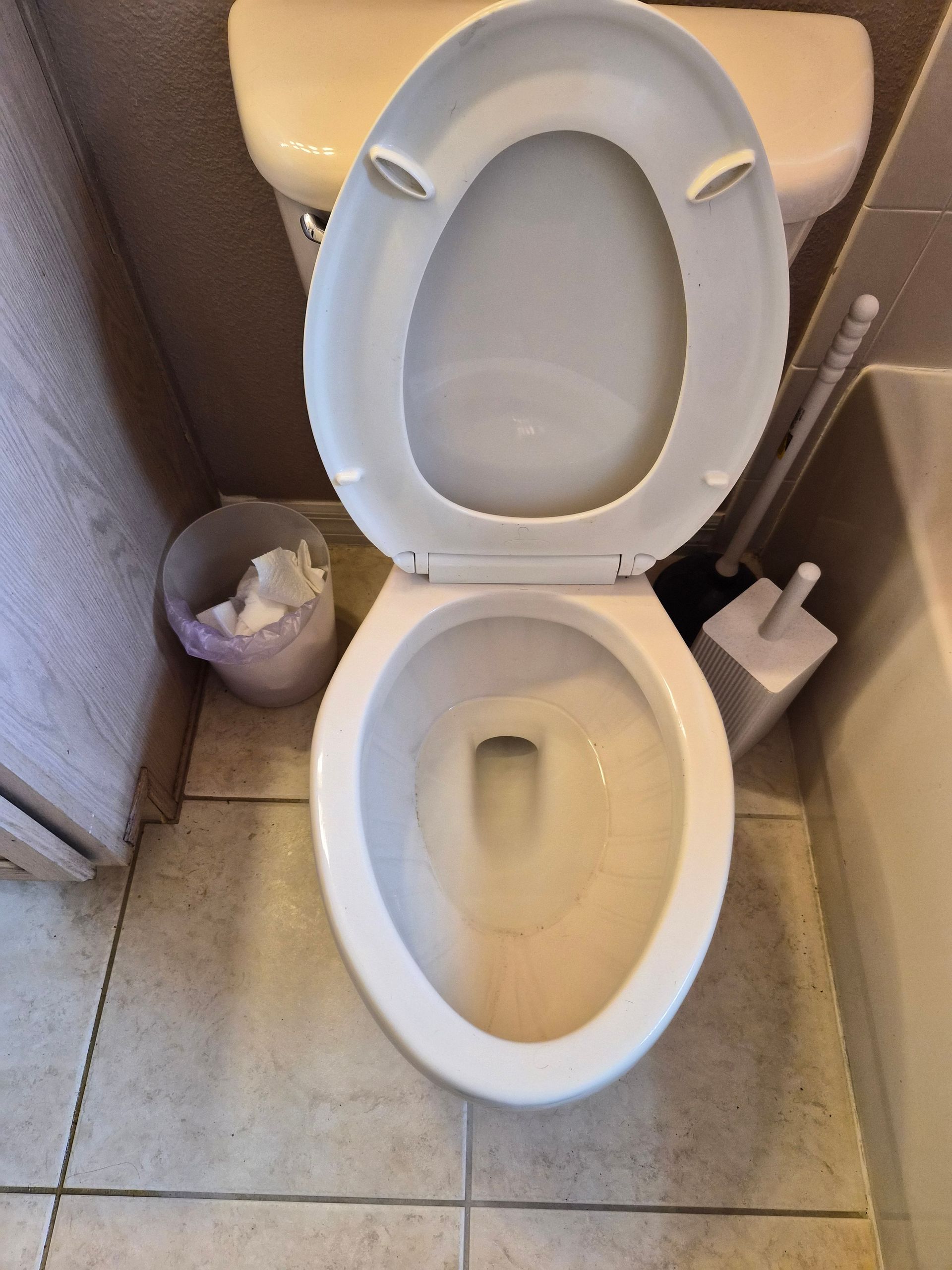 Open toilet in a small tiled bathroom stall with a trash can beside it