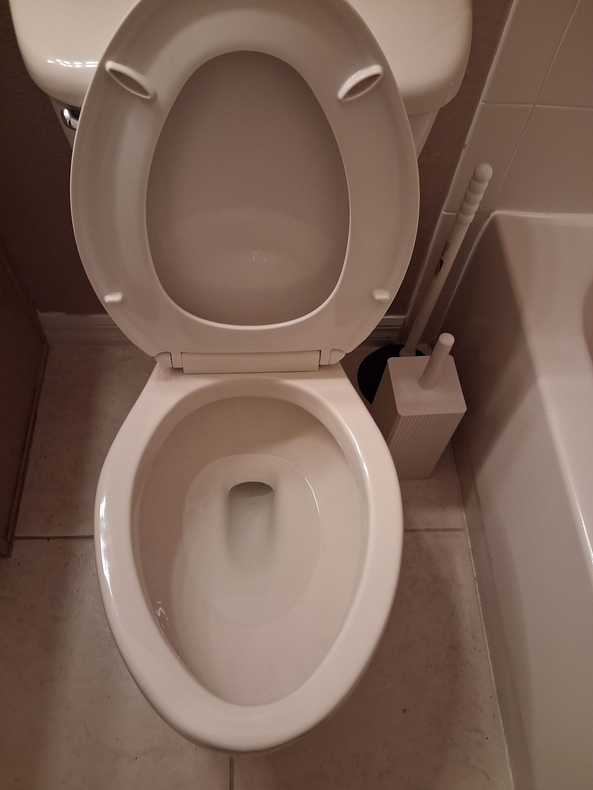 Open toilet seat in a small bathroom with beige tiles and a toilet paper holder nearby