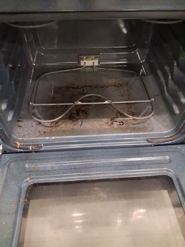 Inside an oven, a wire rack sits above a dirty lower tray with food crumbs.