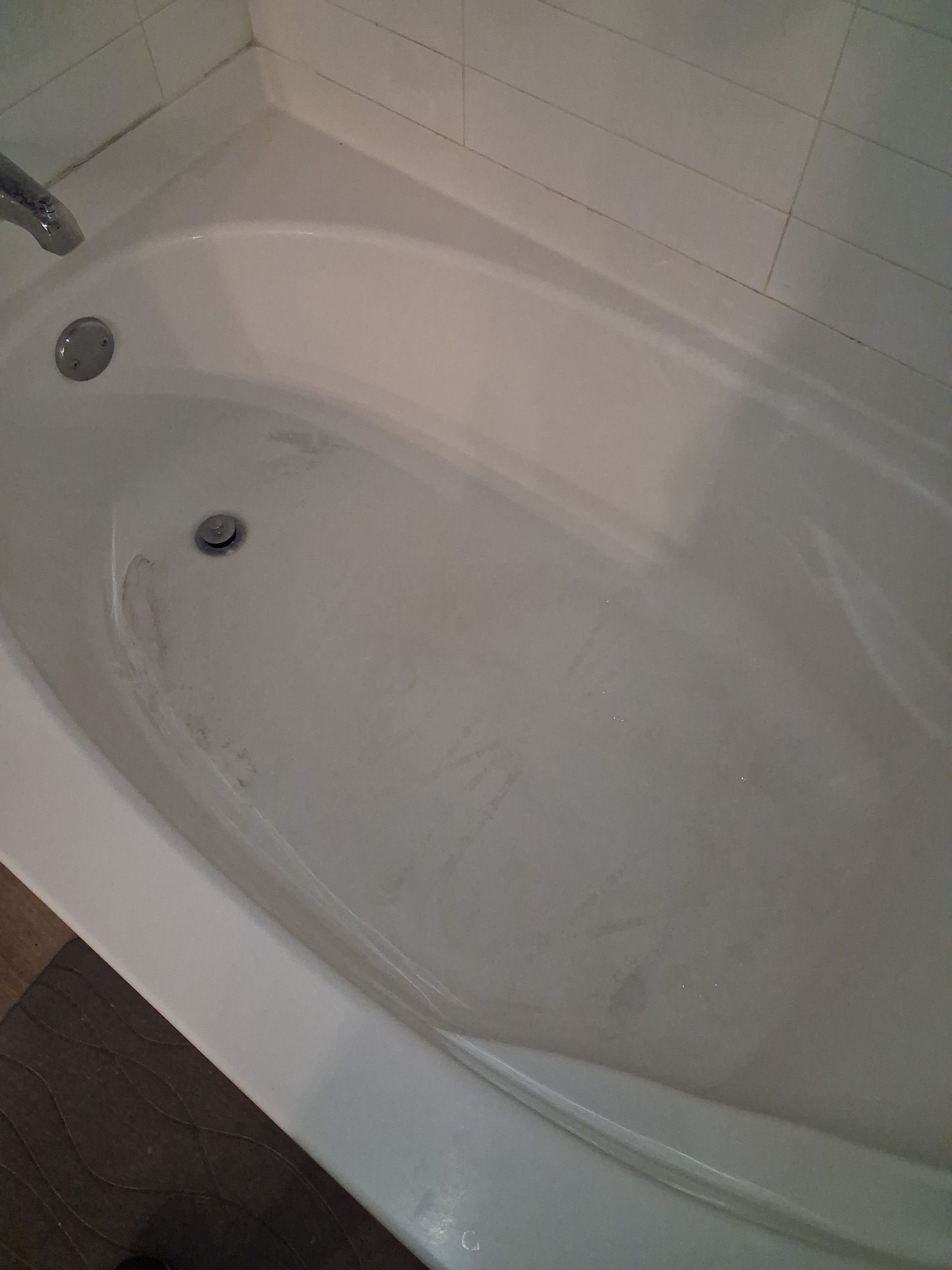 White bathtub with shower wall and drain visible, viewed from above
