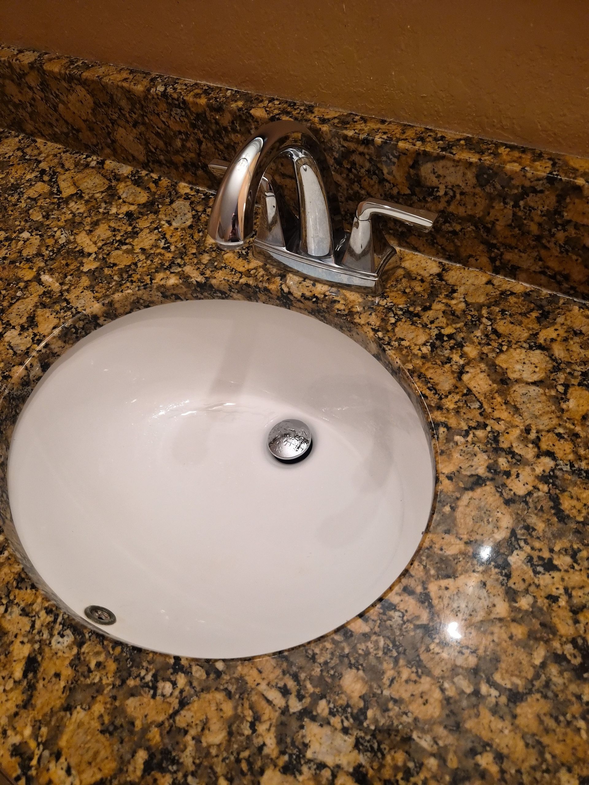 Bathroom sink with chrome faucet and brown granite countertop.