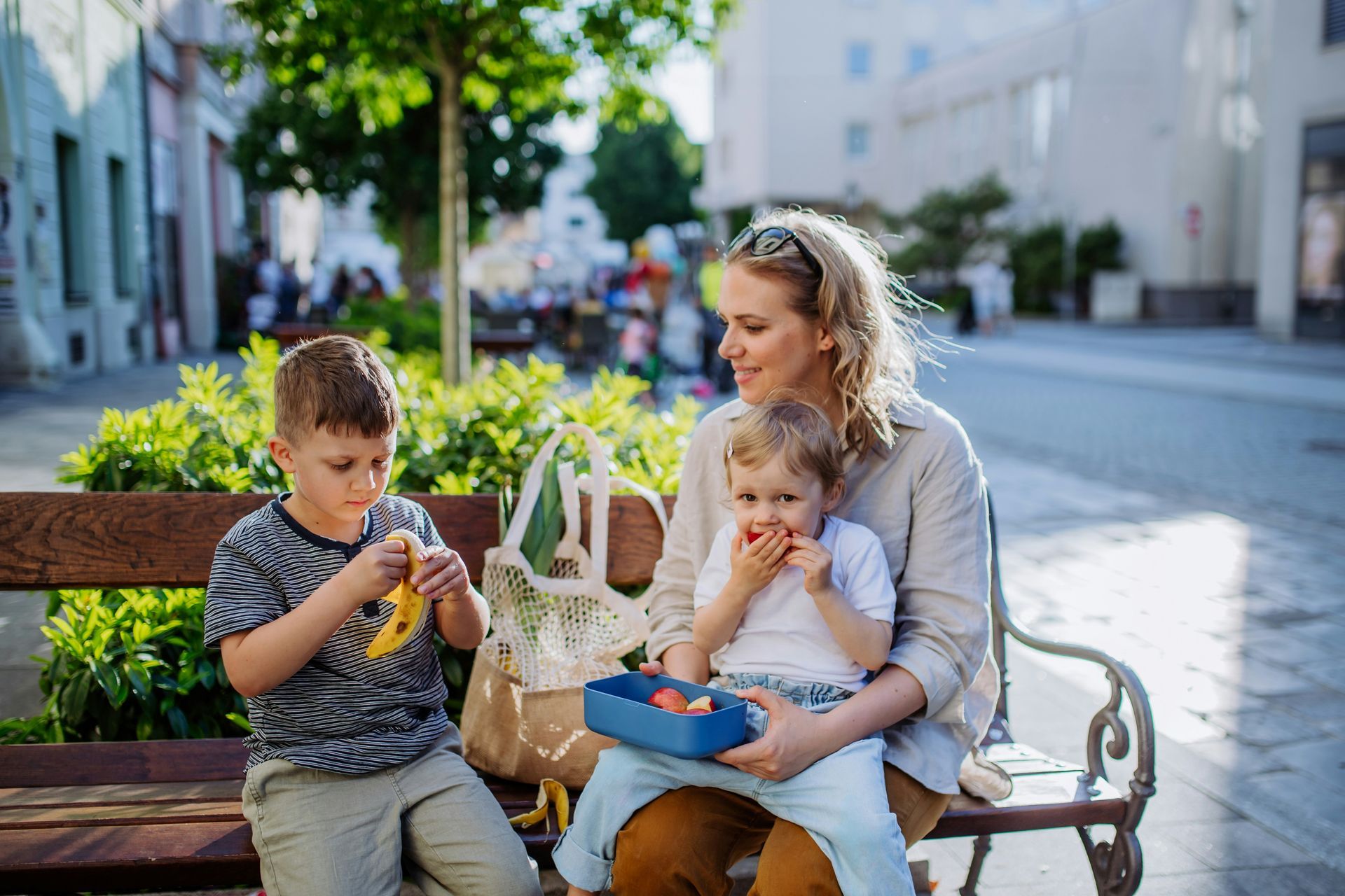 Woman with two children eating fruit on a park bench.