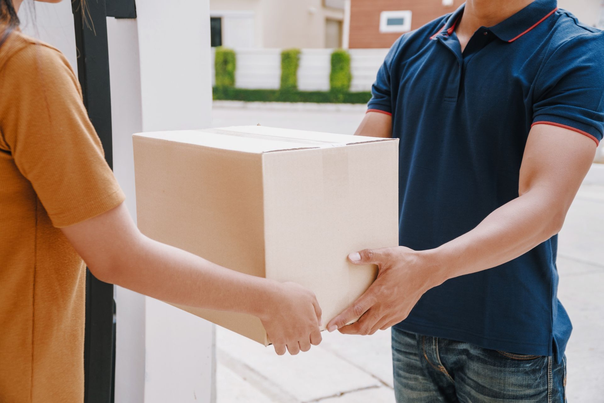 Two people handing off a cardboard box outdoors near a building entrance