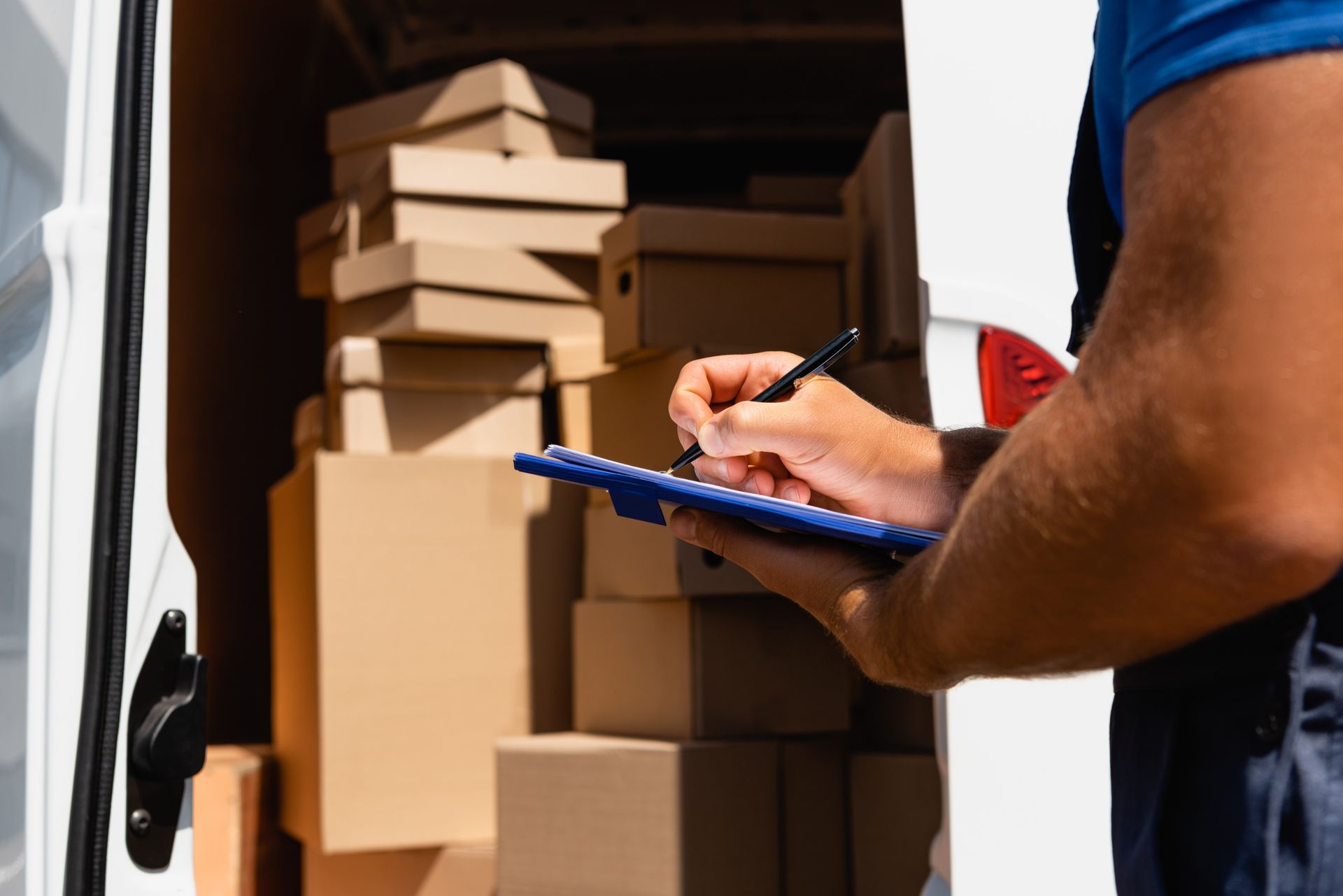 Courier checking a clipboard beside stacked cardboard boxes in a delivery van