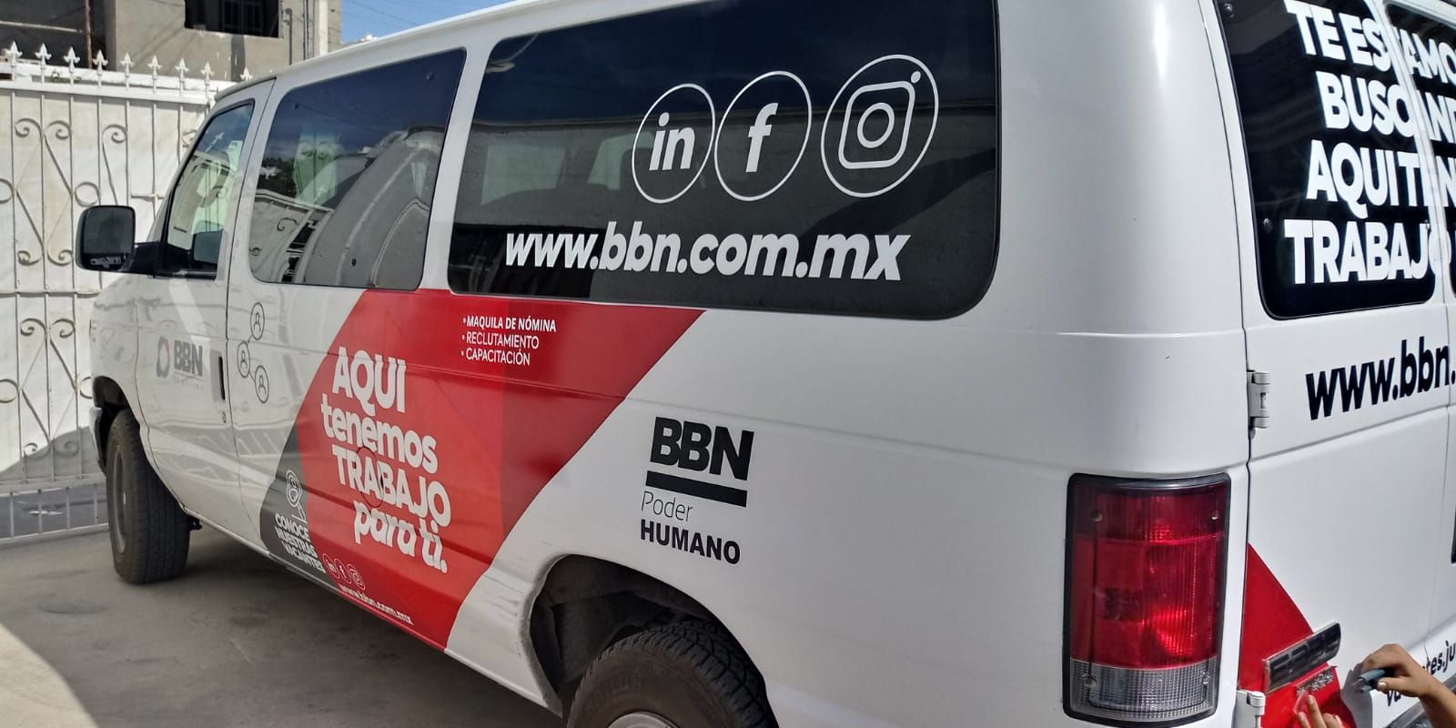 Una camioneta blanca con una franja roja en el costado está estacionada frente a un edificio.