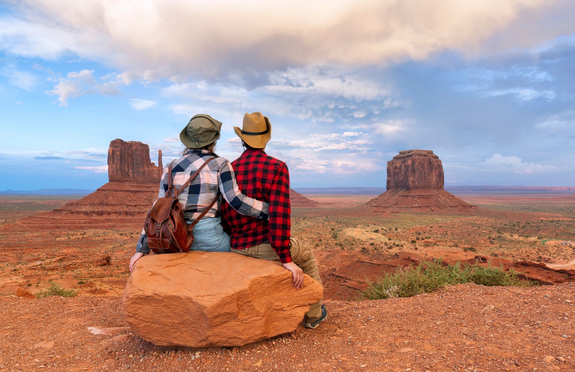 A man and a woman are sitting on a rock in the desert.