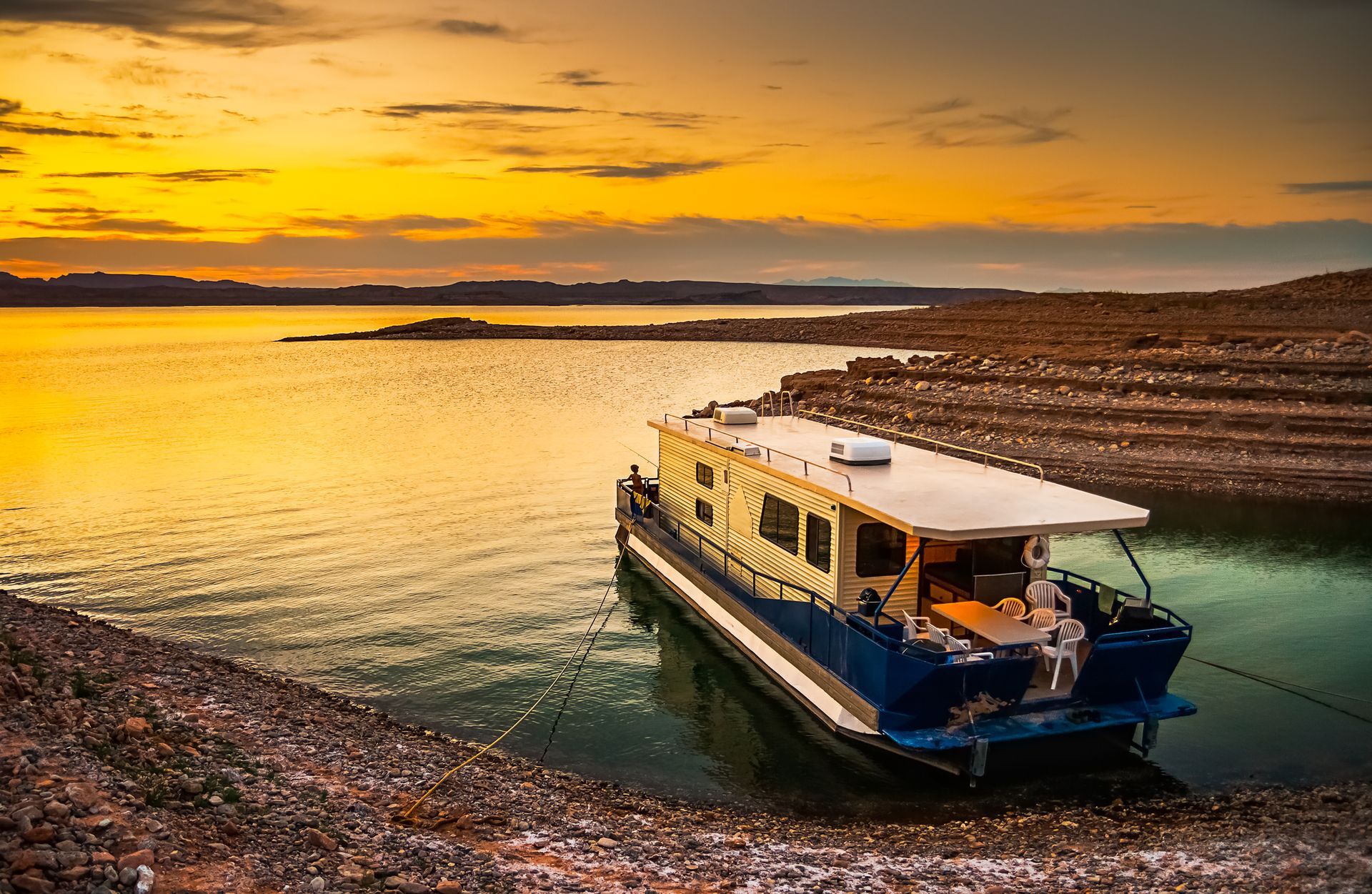 A houseboat is docked on the shore of a lake at sunset.