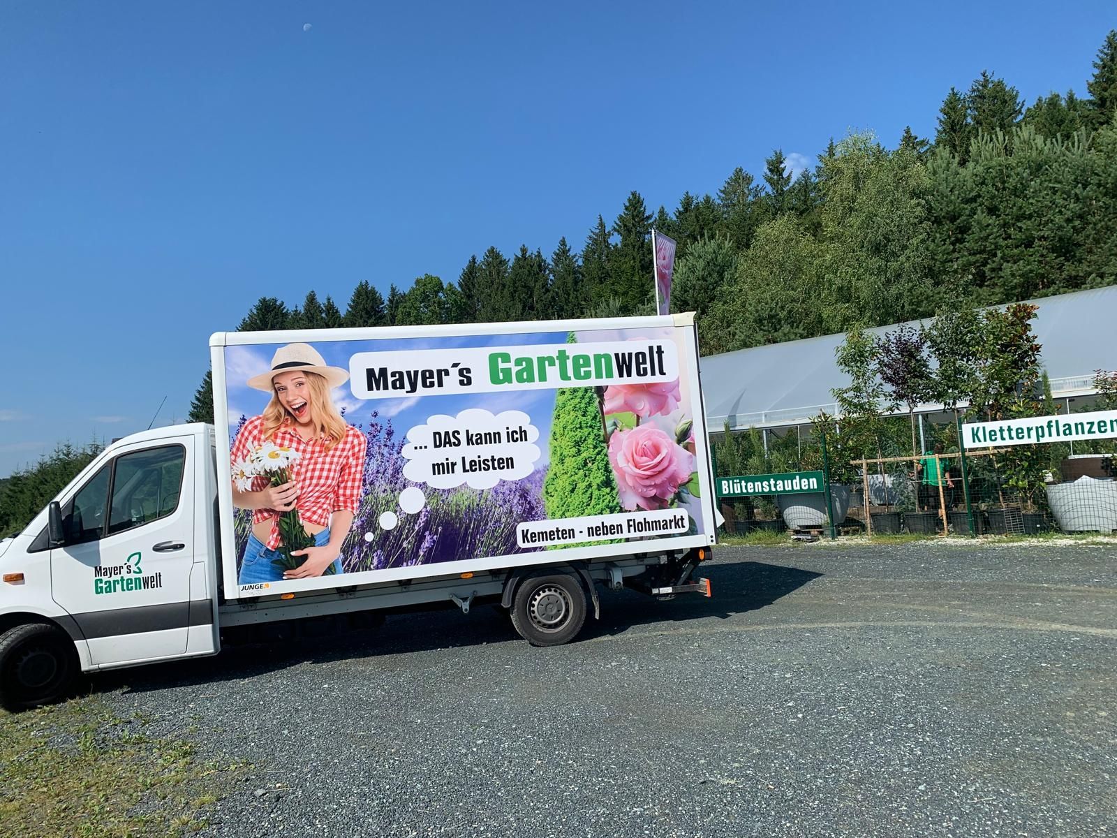 Ein weißer Lastwagen mit einer großen Werbung an der Seite steht auf einem Schotterplatz.