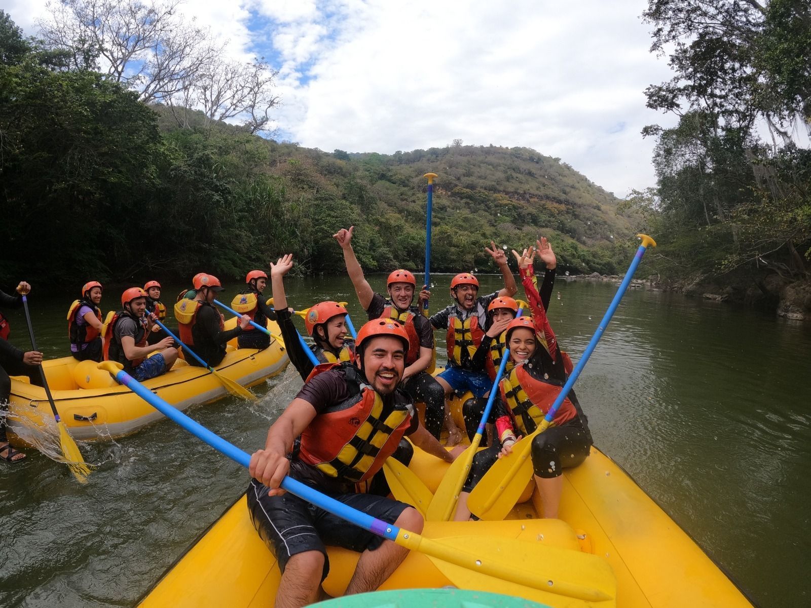 Grupo de rafting en botes amarillos en un río, sonriendo y levantando los remos en un cañón boscoso