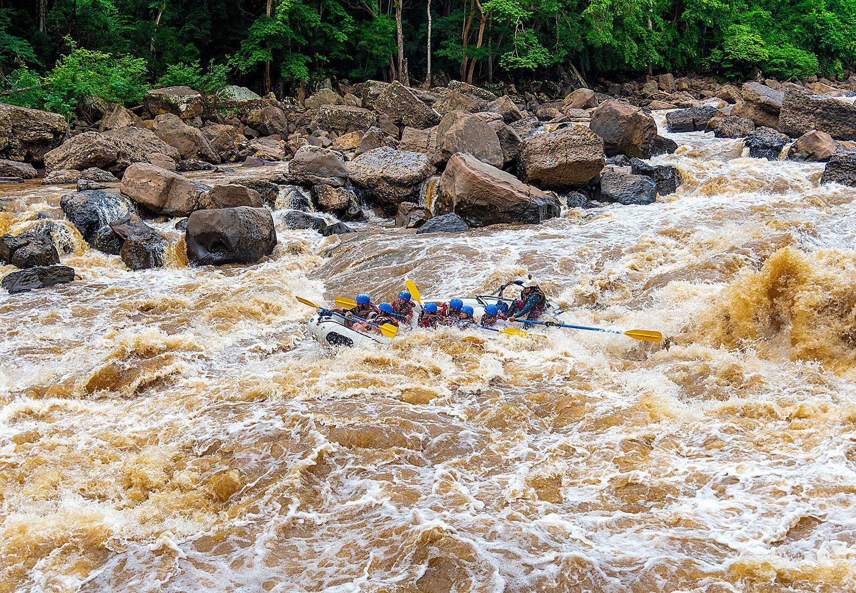 Grupo con cascos naranjas y chalecos salvavidas haciendo rafting en una balsa inflable amarilla por un río