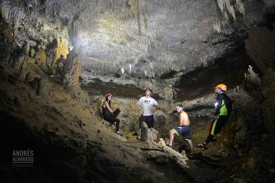 Tres excursionistas cruzan rocas sobre una poza de color turquesa en un estrecho cañón forestal.