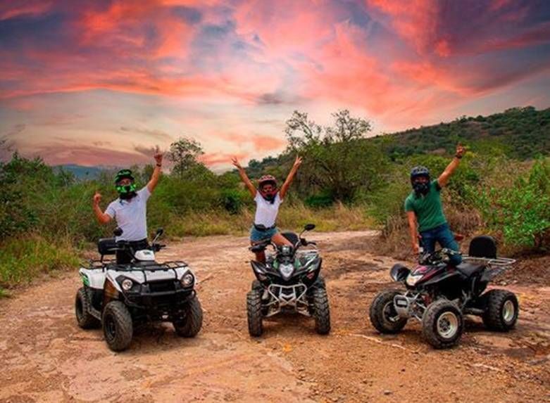 Tres personas en cuatrimotos recorren un sendero de tierra con los brazos en alto.