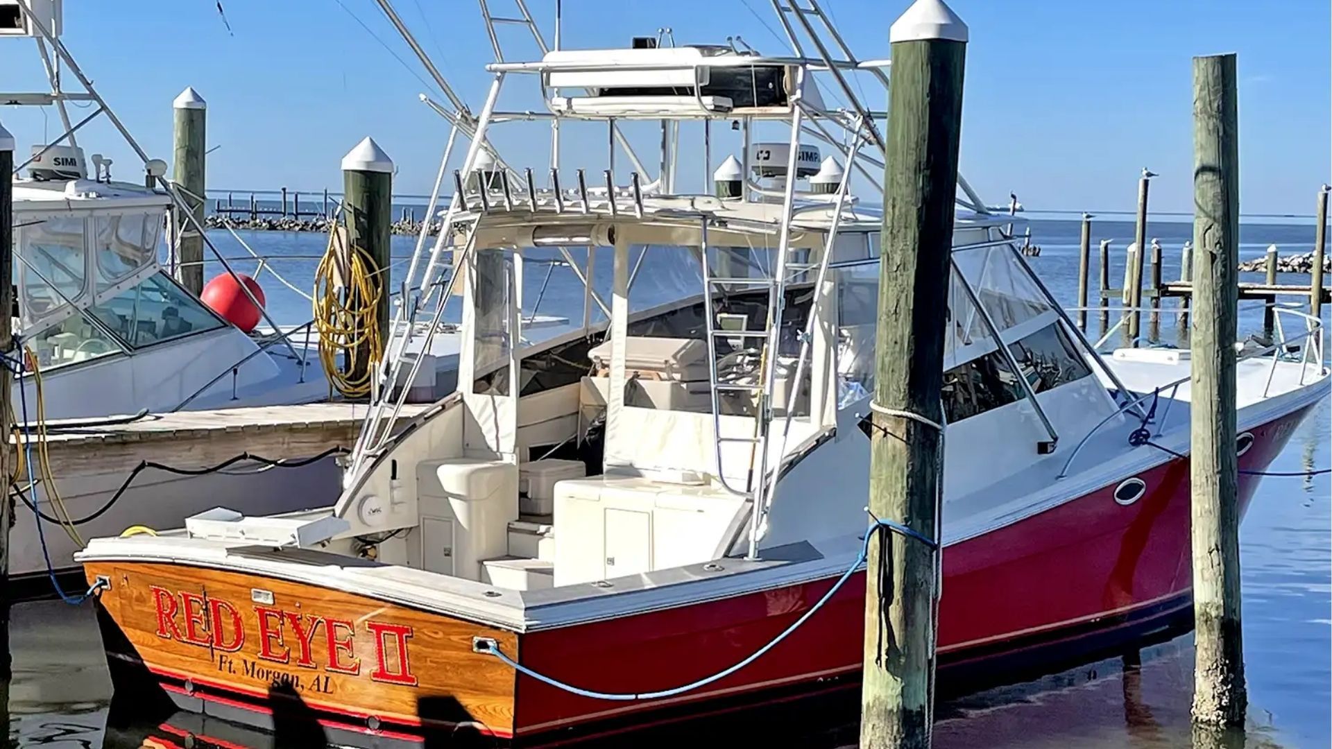 A red and white boat named "RED EYE V" with a wood transom, docked at a pier on a sunny day.