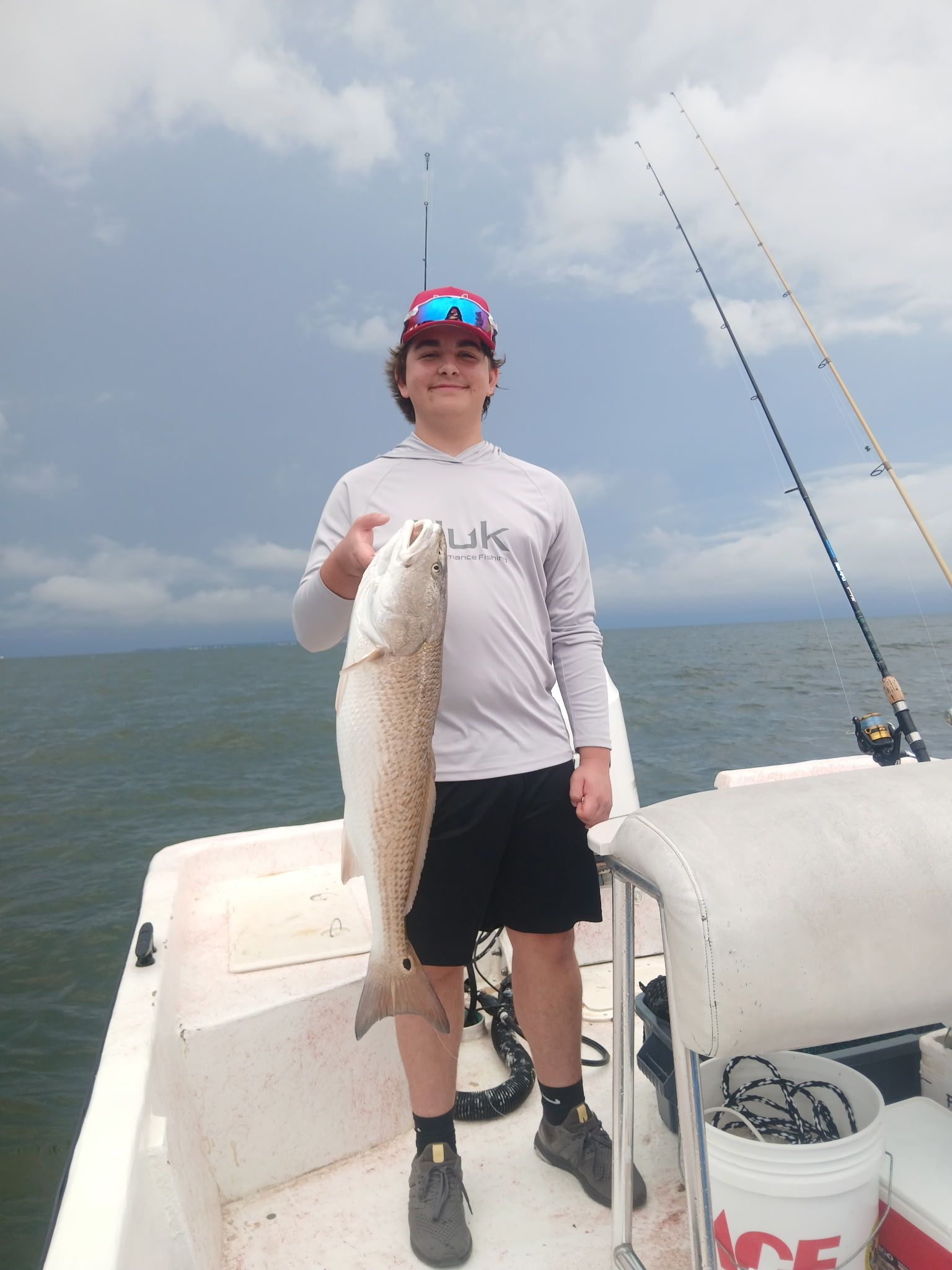 Person on a boat holding a large fish, with fishing rods and cloudy water in the background.