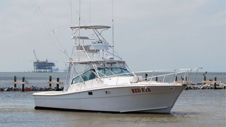 A white sport fishing boat named "RED EYE" anchored in water with an oil platform in the distance.