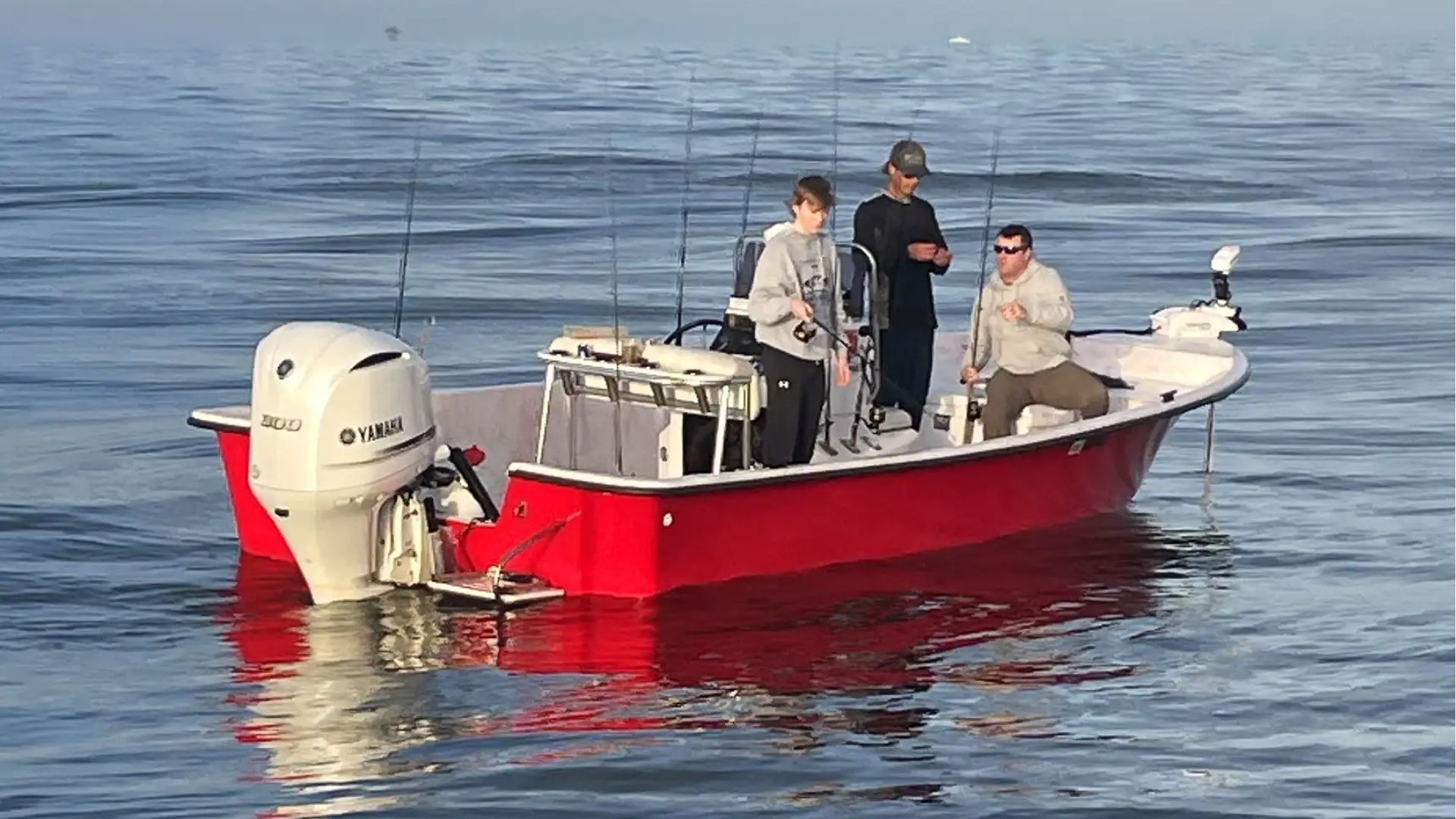 Three people fishing from a red boat on calm, open water.