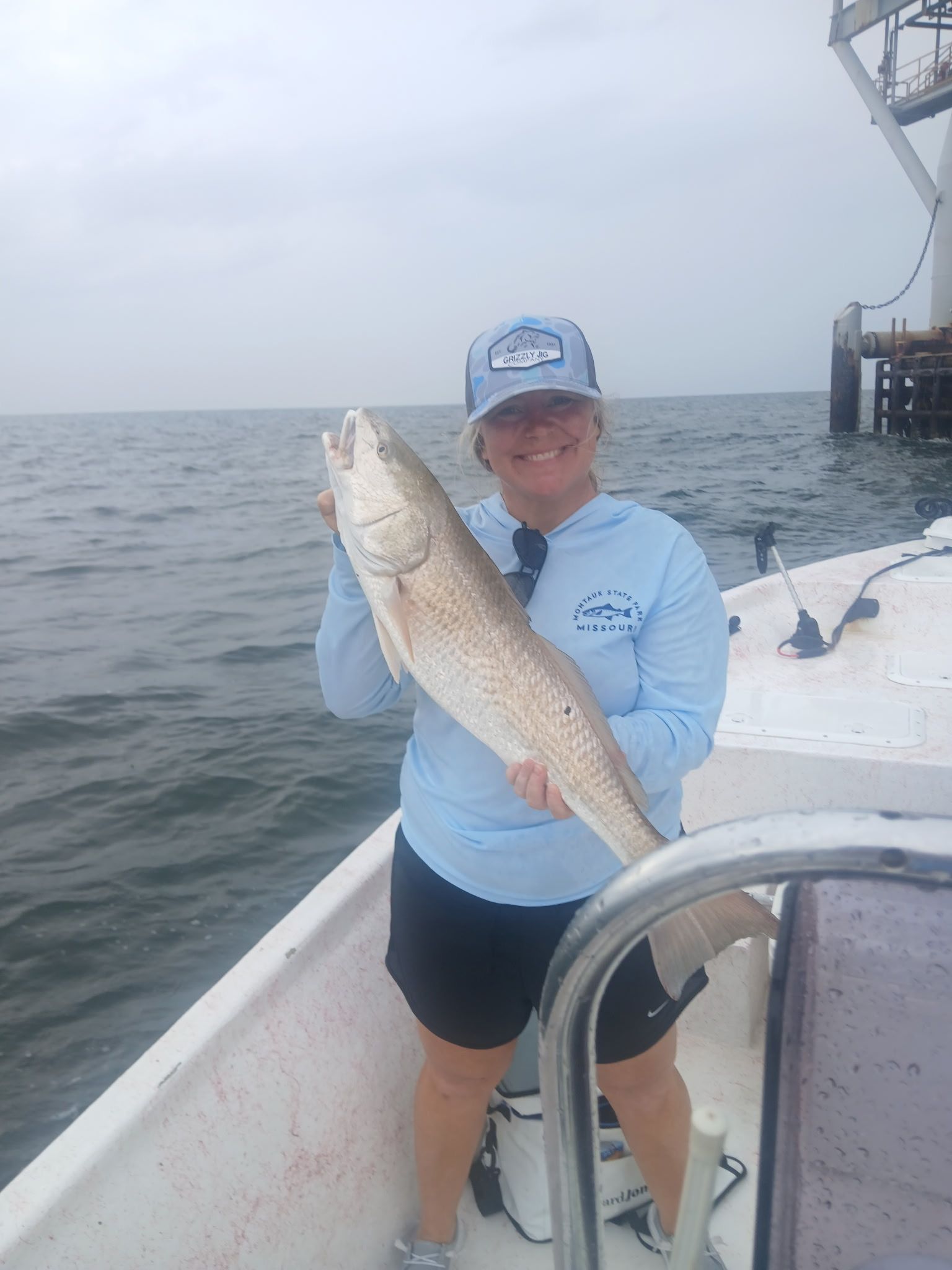 Person on a boat holding up a large fish on a cloudy day
